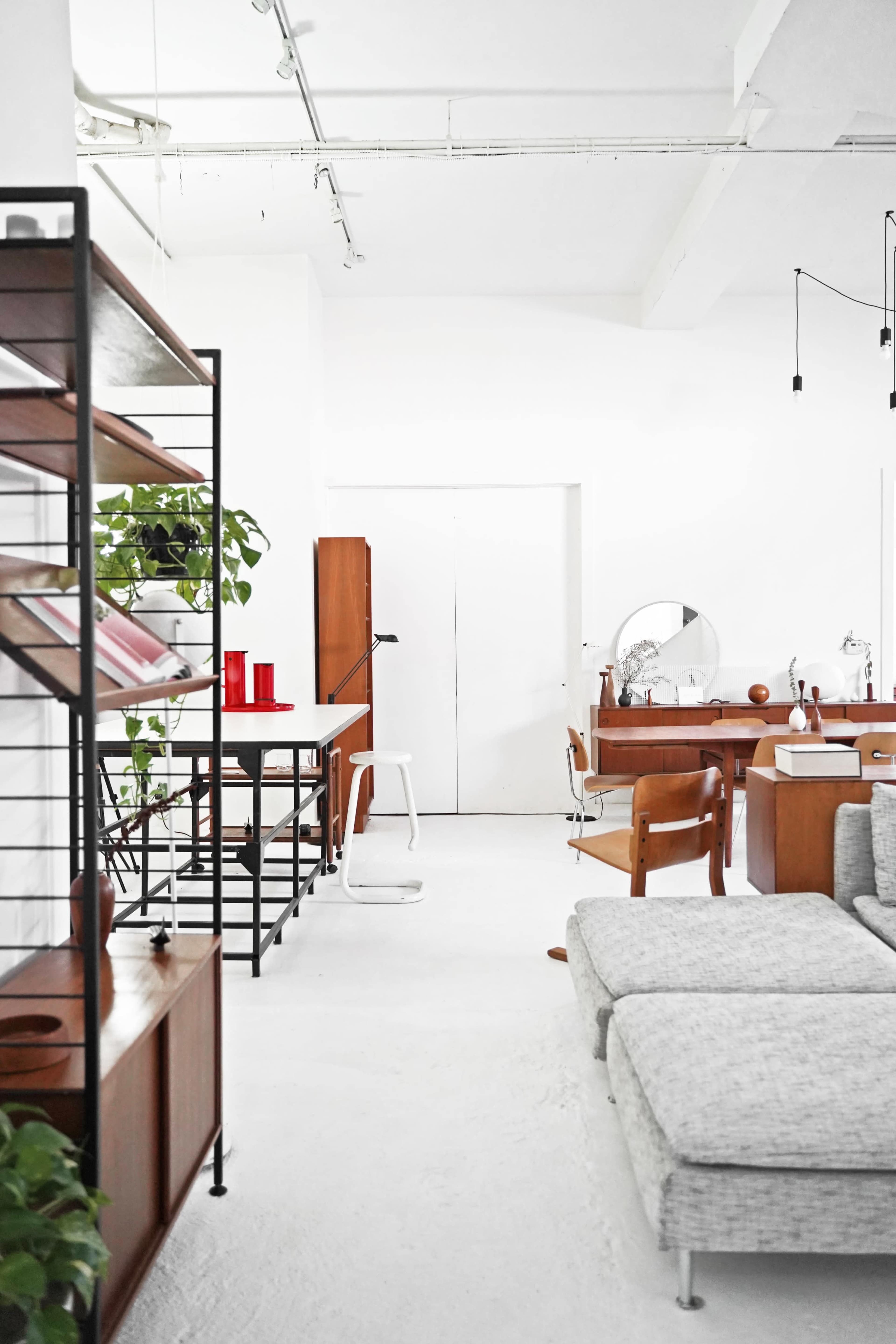 A modern, open-concept interior featuring a mix of wooden furniture, a minimalist shelving unit, and greenery.
