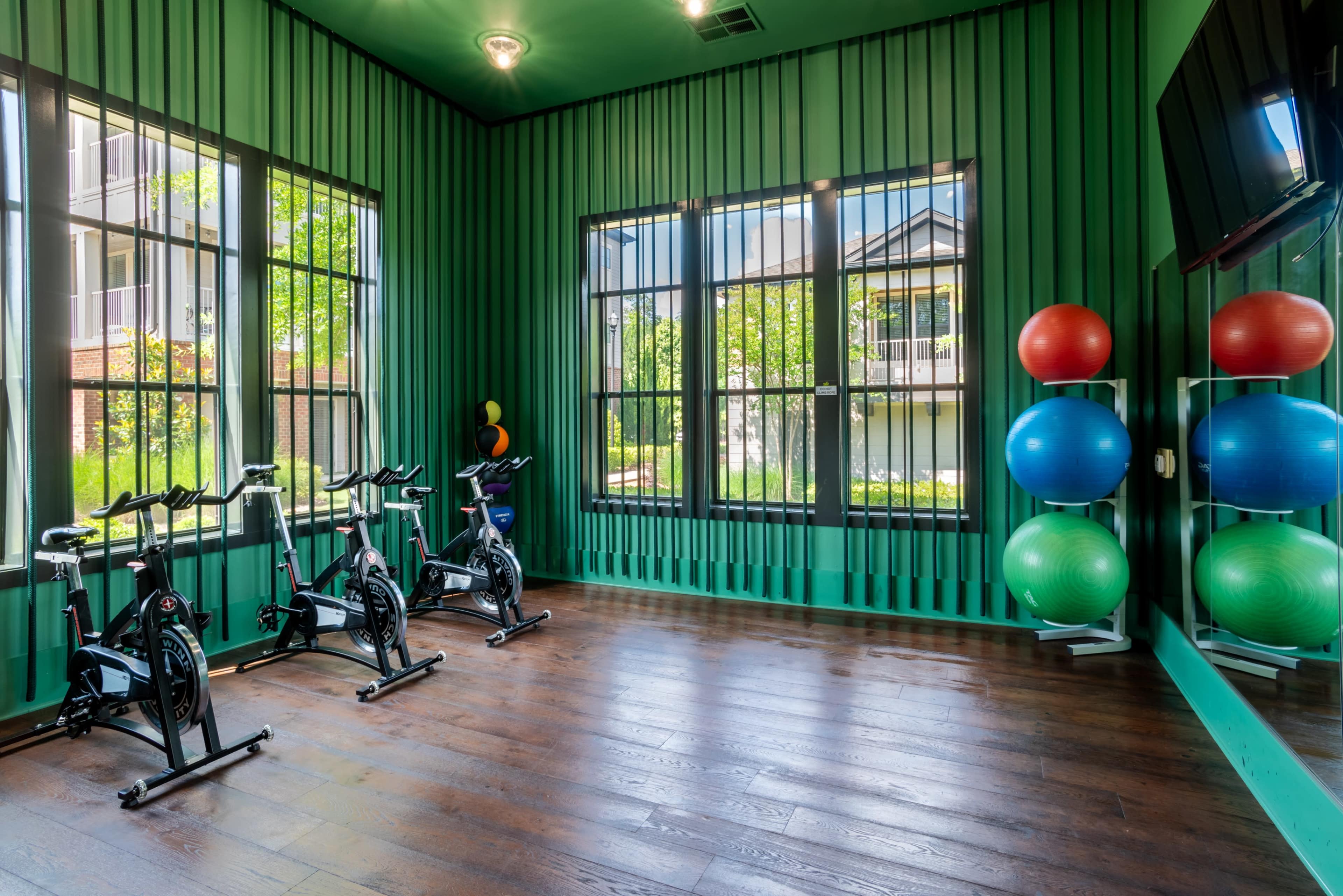 A bright green fitness room with exercise bikes and exercise balls arranged neatly against the walls.