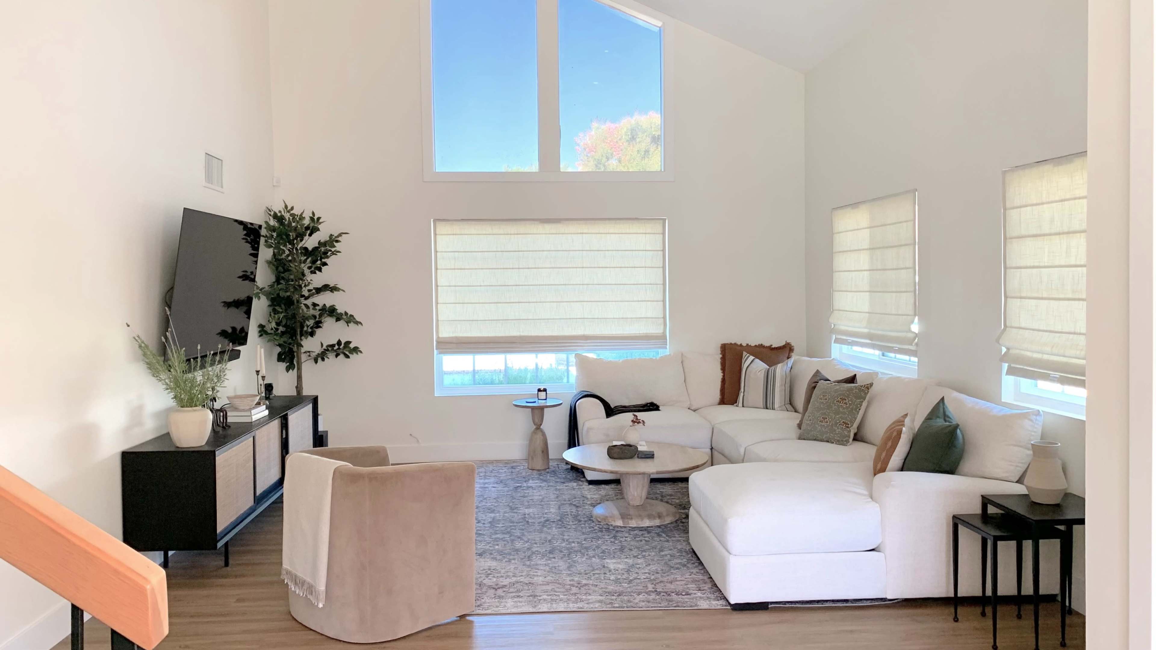 A modern living room with a white sectional sofa, a coffee table, and large windows allowing natural light to enter.