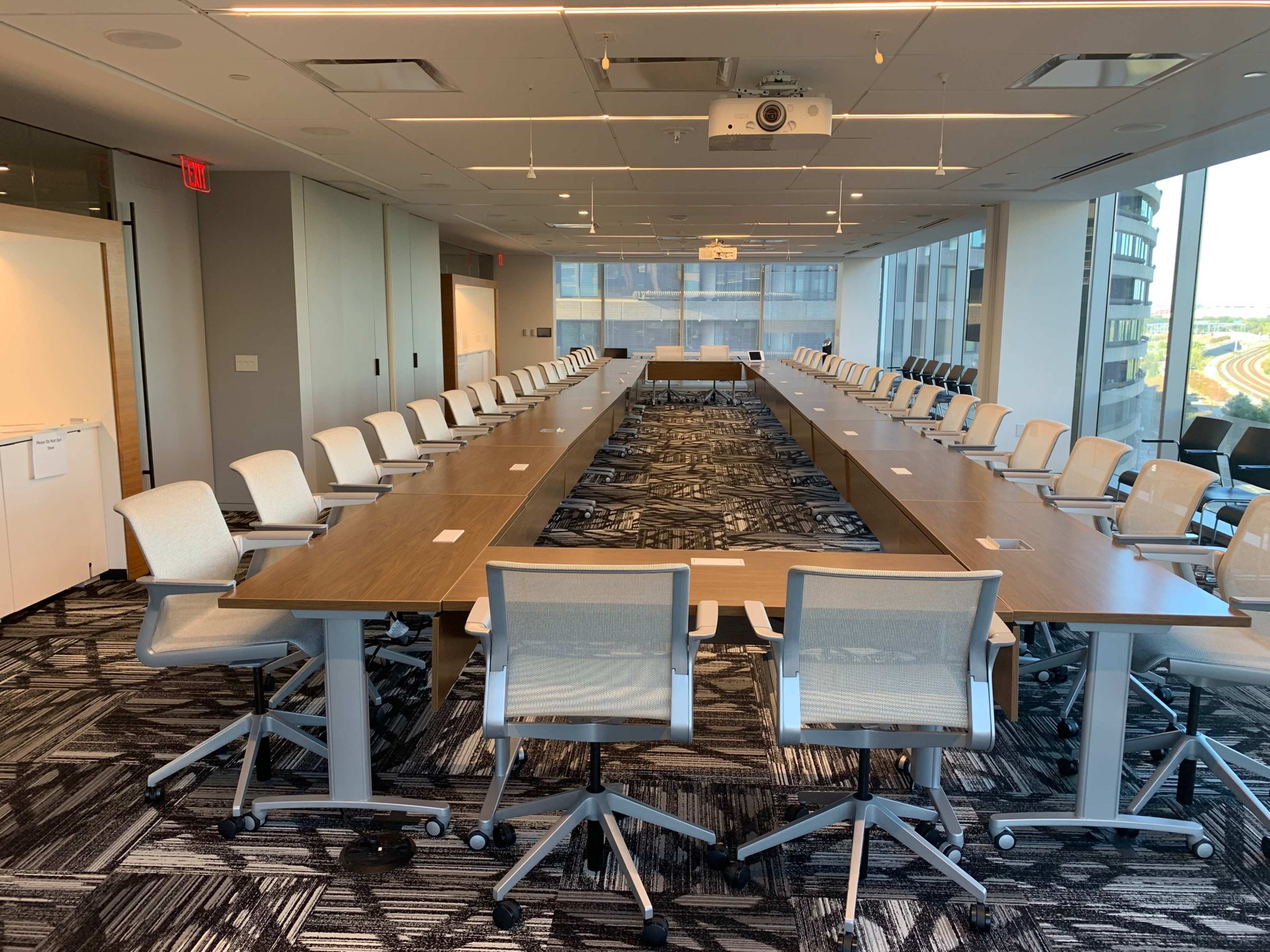 A large conference room with a long, rectangular table surrounded by swivel chairs and large windows providing natural light.