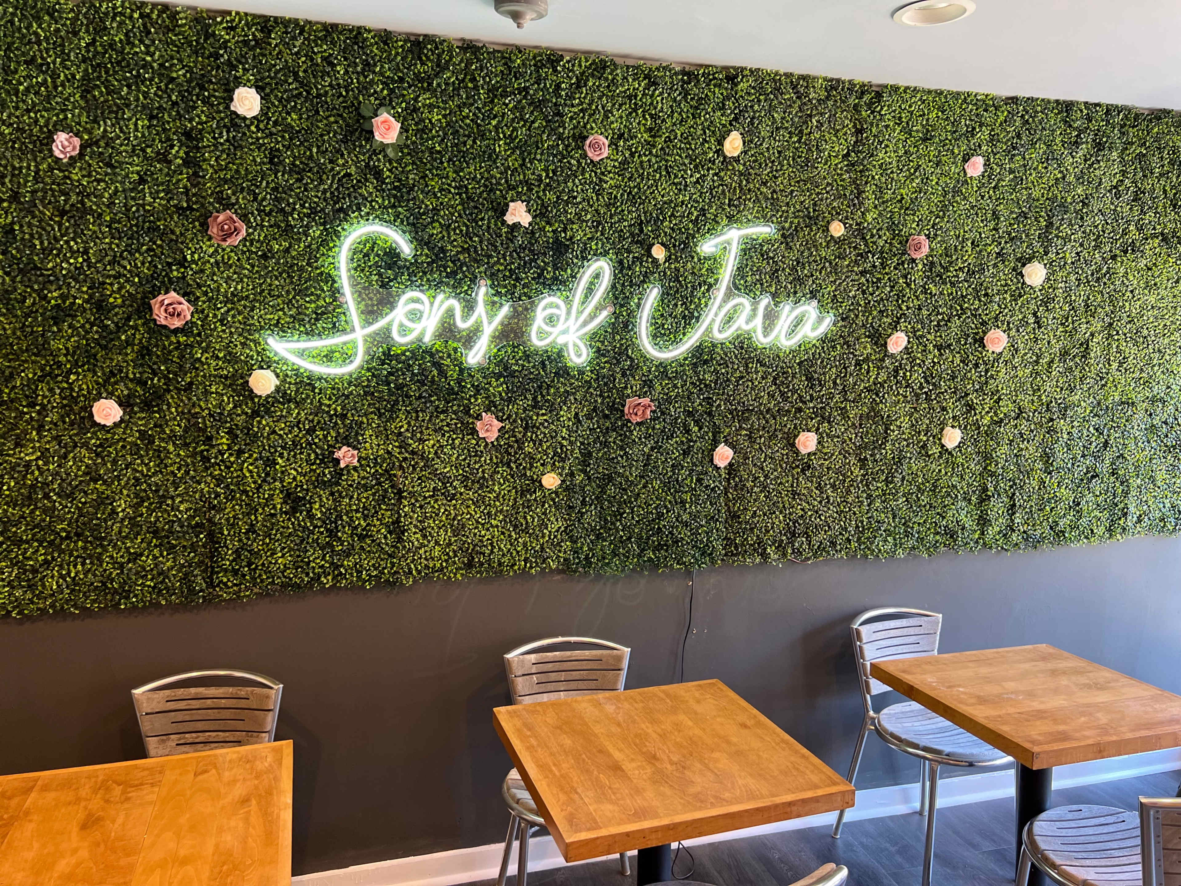 A café interior with a wall covered in greenery and neon signage that reads "Song of Java."