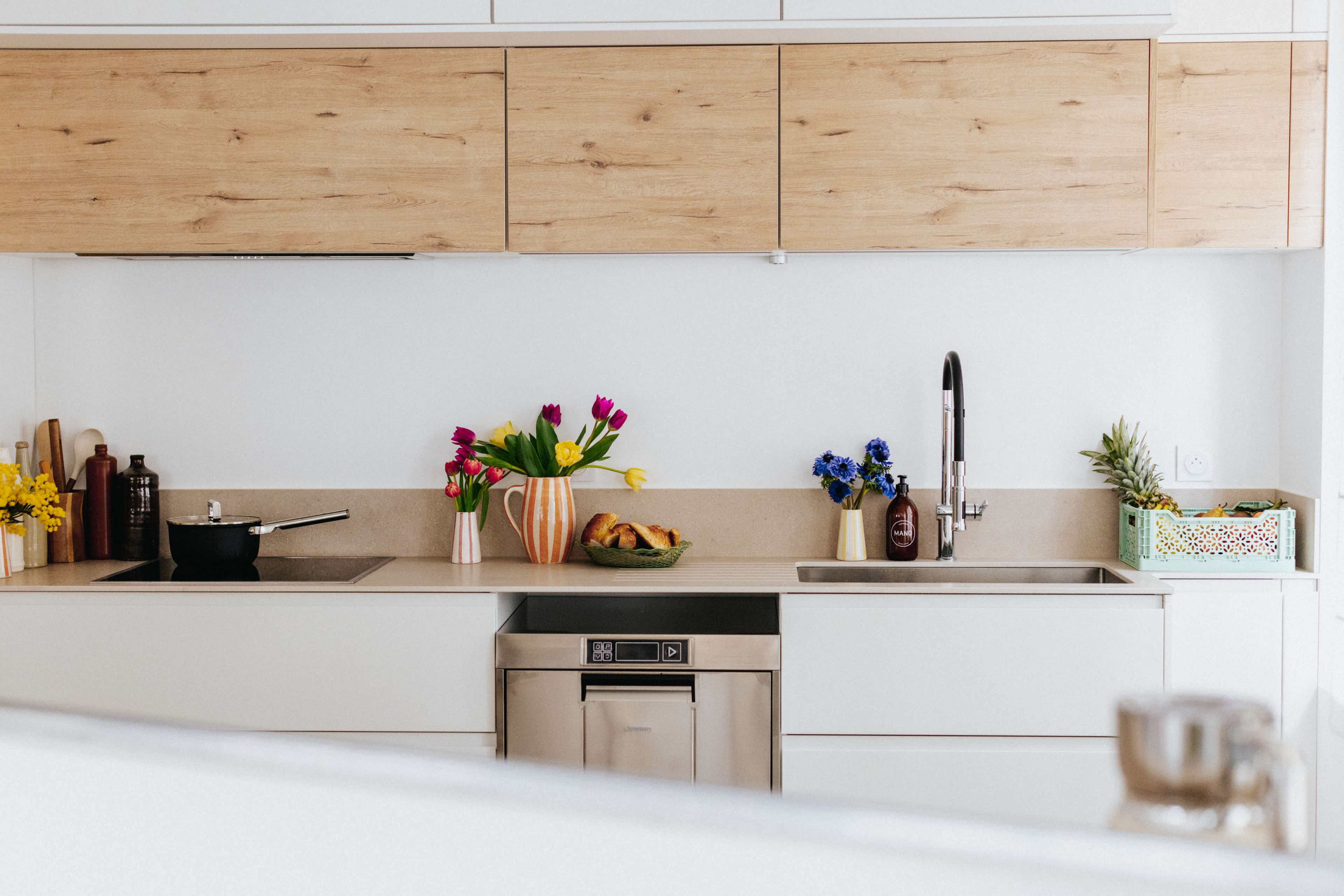 A modern kitchen features wooden cabinets, stainless steel appliances, and a variety of colorful flowers in vases on the countertop.