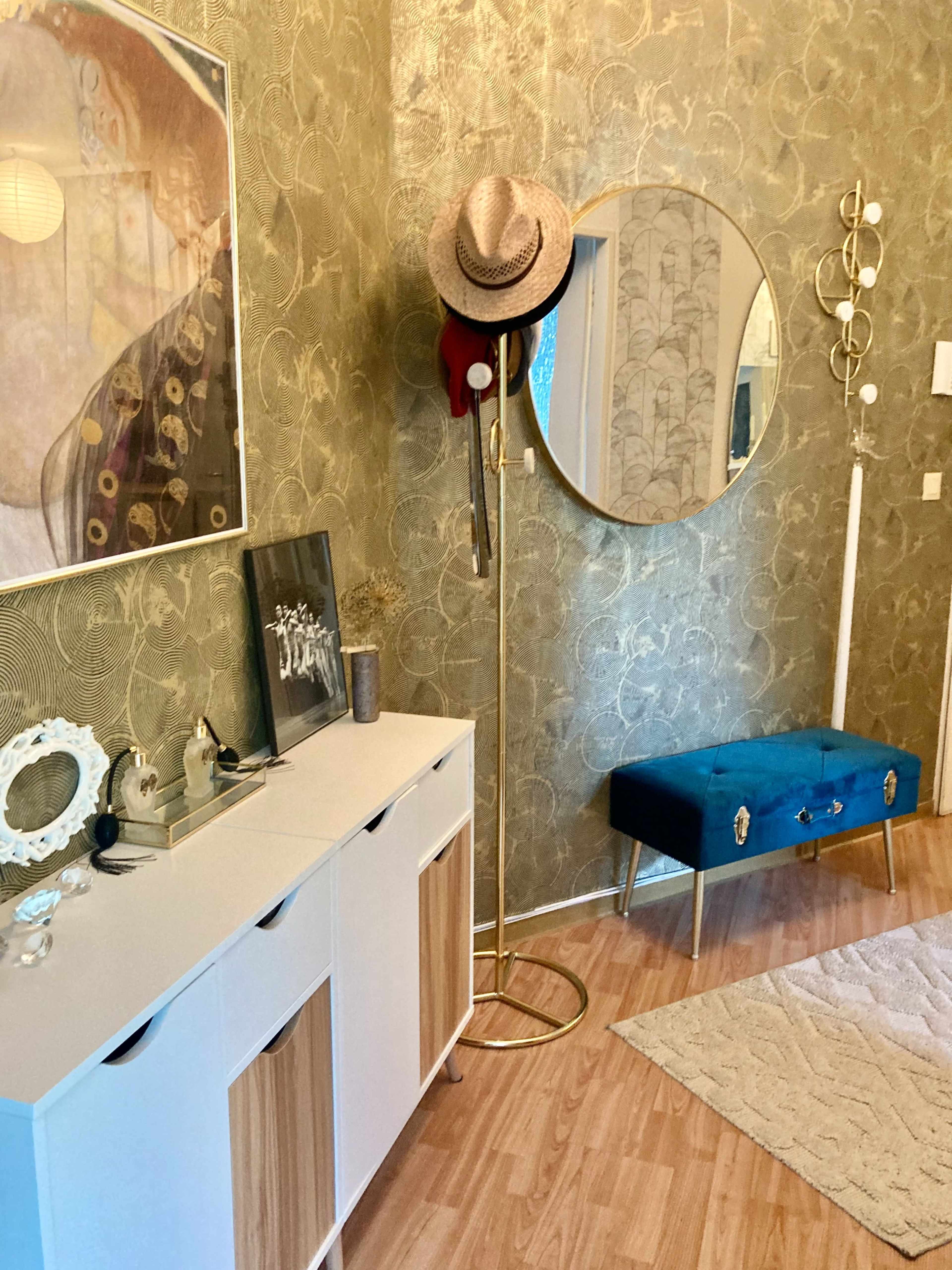 The image shows a stylish entryway featuring a white and wood storage cabinet, a round mirror on the wall, a hat rack with accessories, and a blue upholstered bench on a wooden floor.