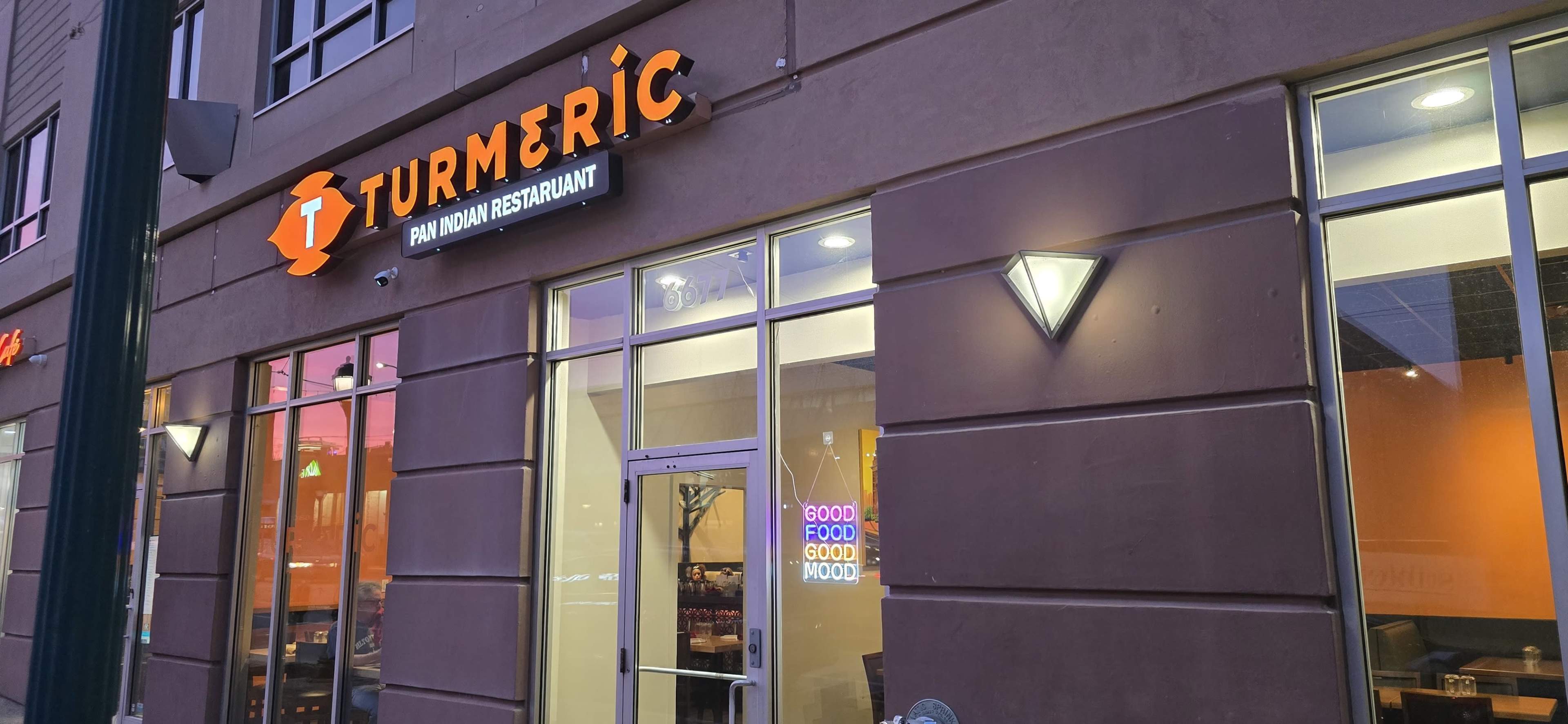 The exterior of a restaurant named "Turmeric" is visible, featuring a modern design with a sign indicating it serves Indian cuisine.