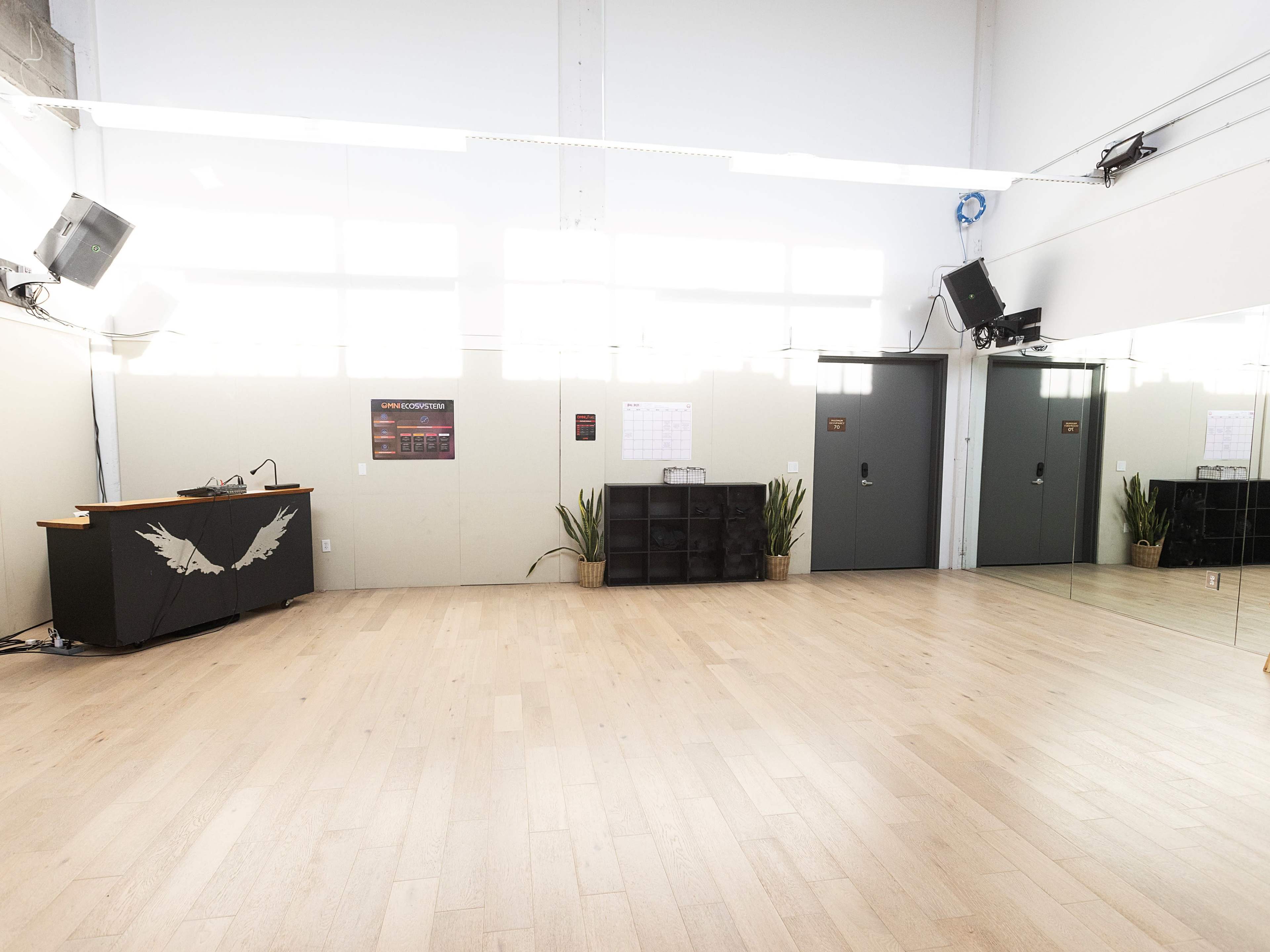 A spacious dance or exercise studio with wooden floors, mirrors on one wall, and a reception area featuring a desk and storage shelves.
