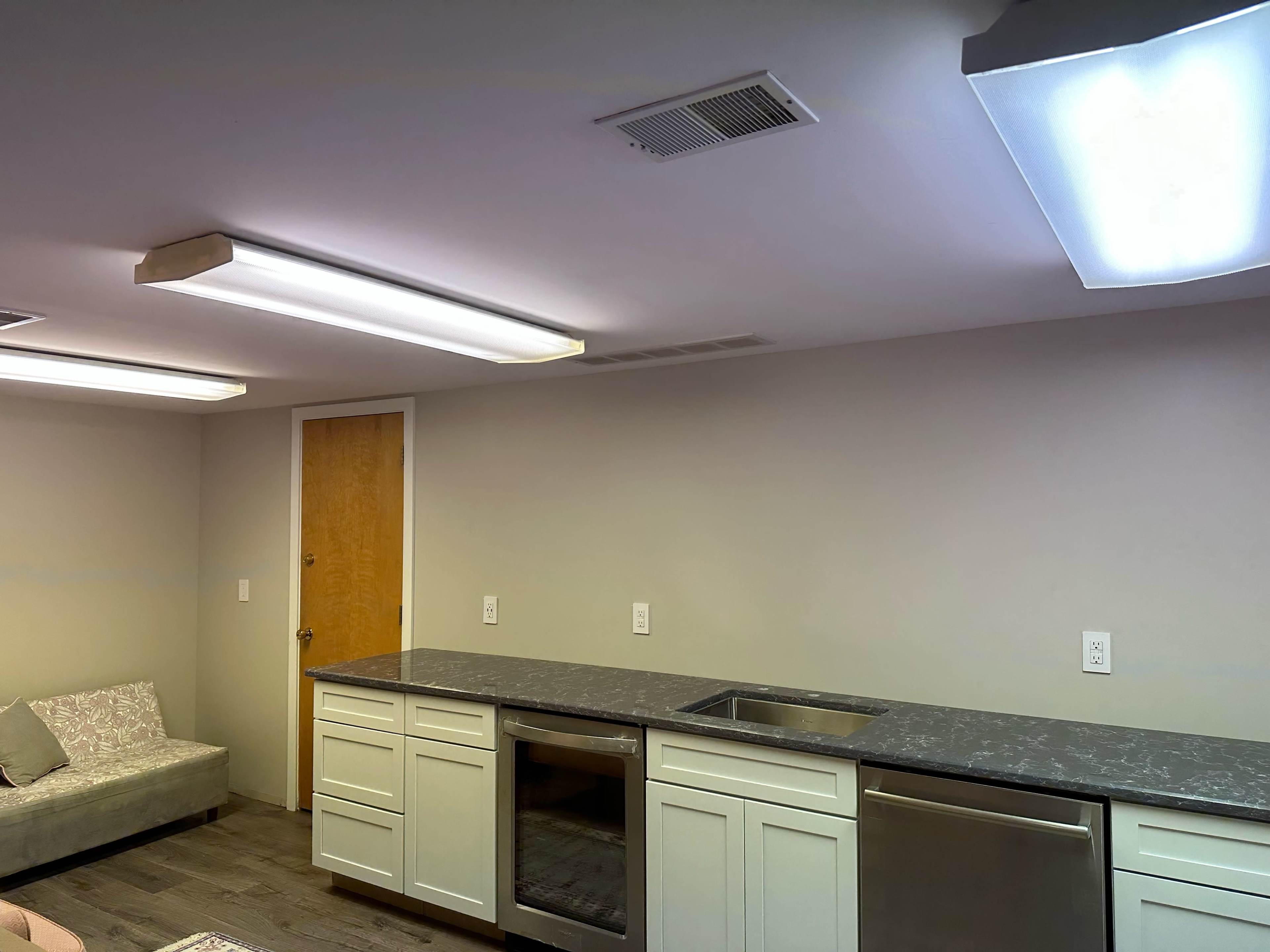The image shows a modern kitchen area with light-colored cabinetry, a gray countertop, and a small sofa in the corner.