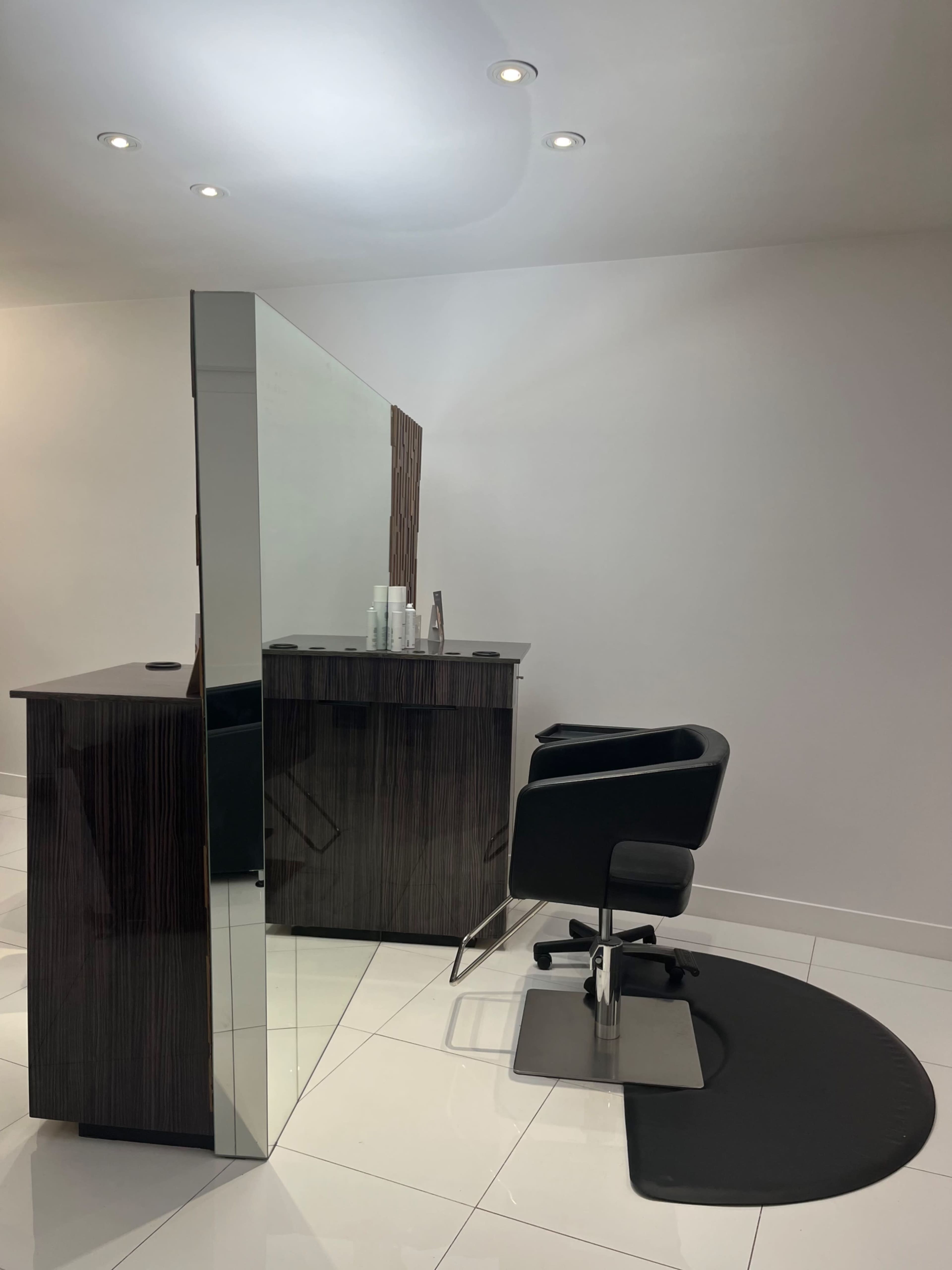 A modern hair salon with a black styling chair and a mirrored partition separating the styling area from the rest of the space.