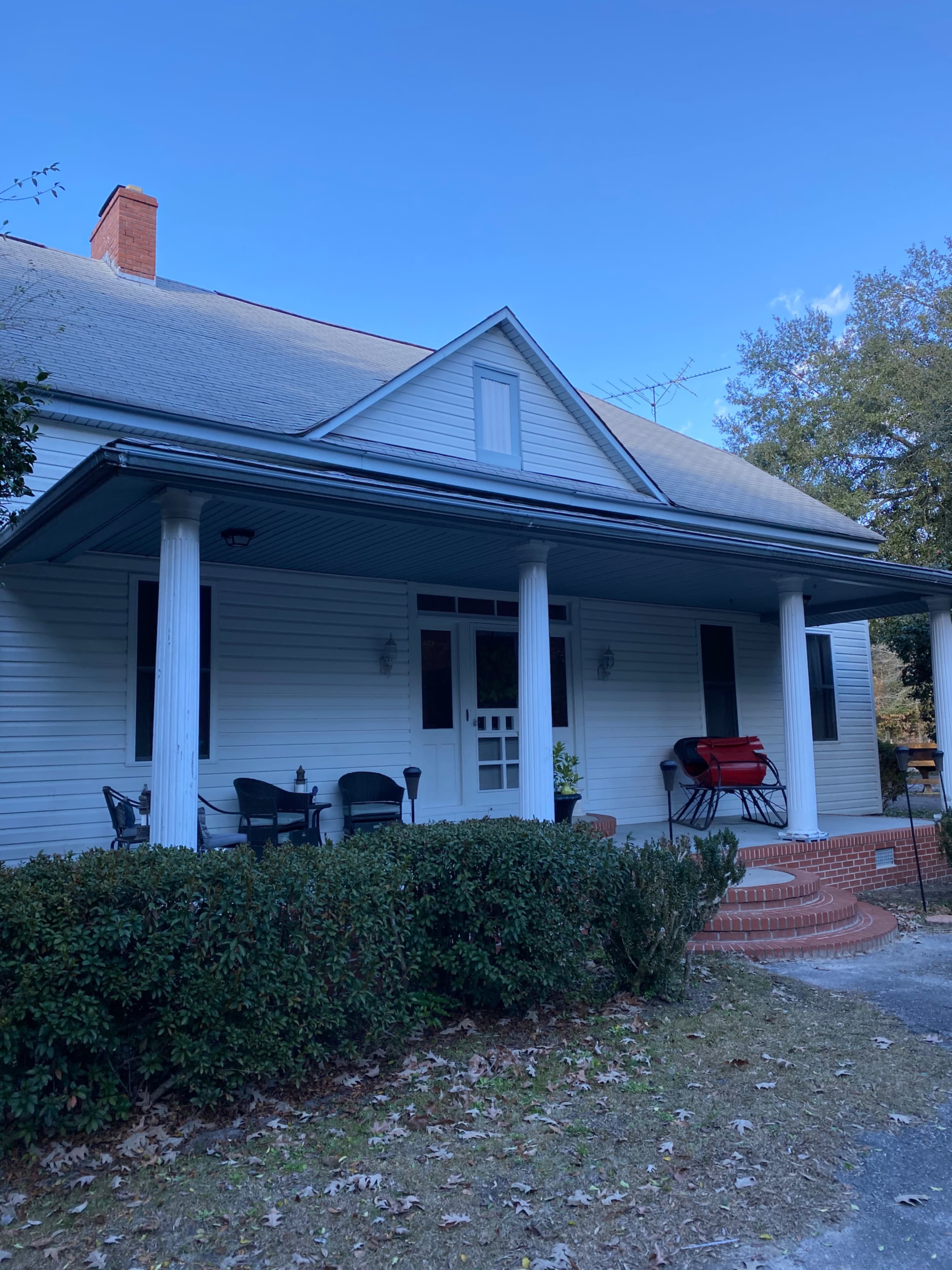 A blue and white house with a large front porch, flanked by columns, and surrounded by trimmed hedges.
