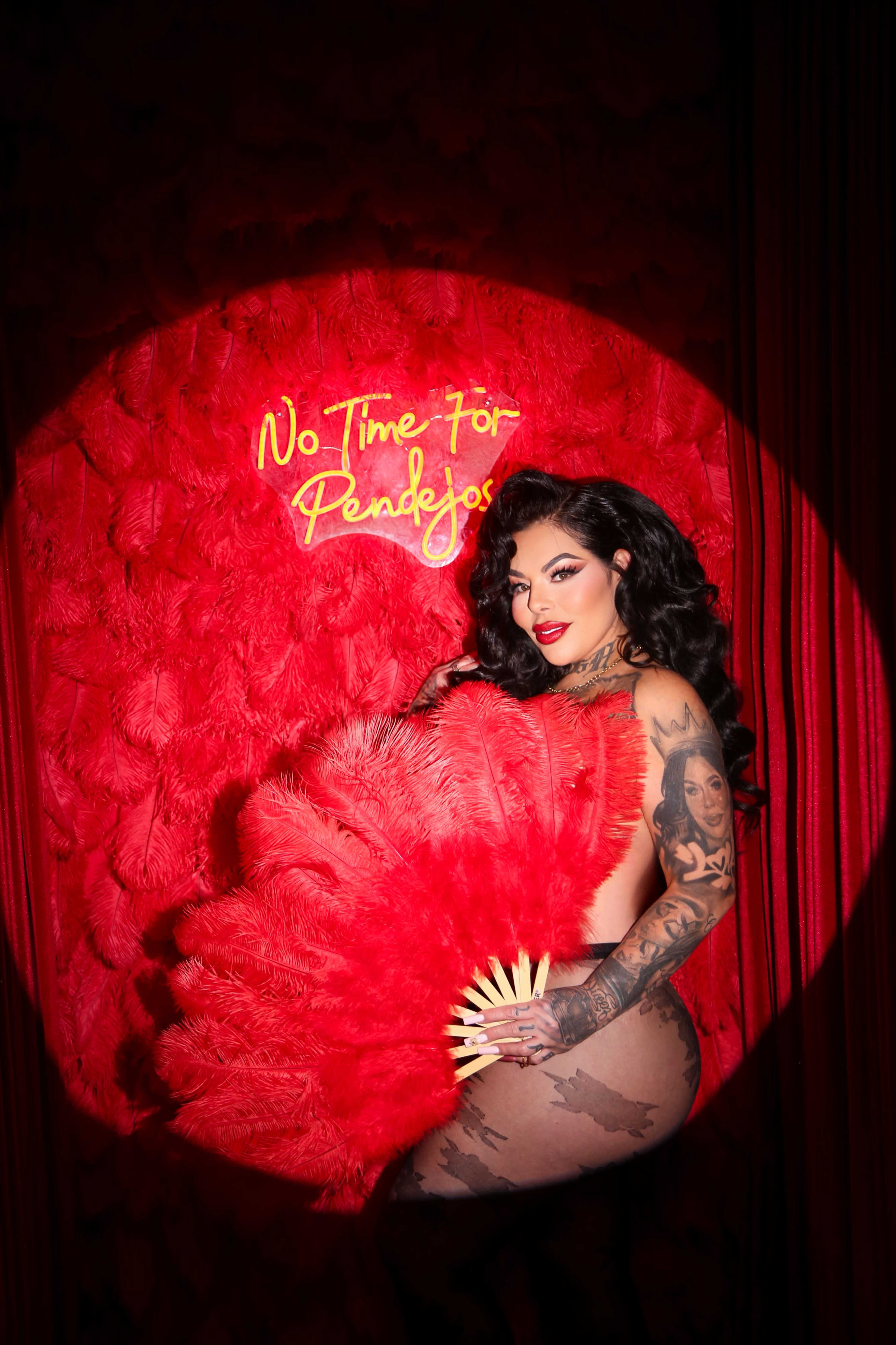 A woman poses with a large feather fan in front of a red textured wall featuring the words "No Time For Regrets."