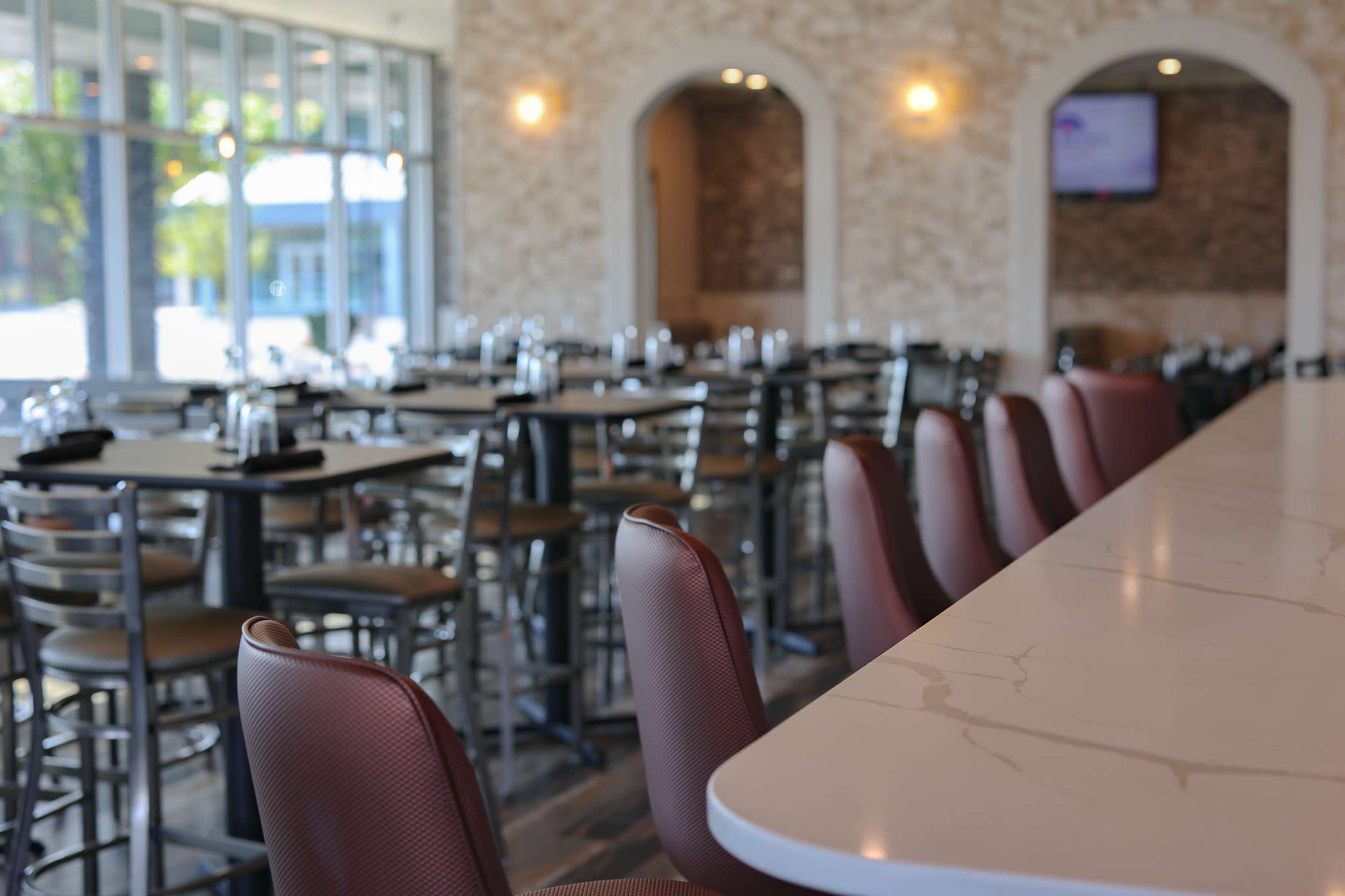 An empty dining area of a restaurant with rows of tables and chairs, and a long marble countertop in the foreground.