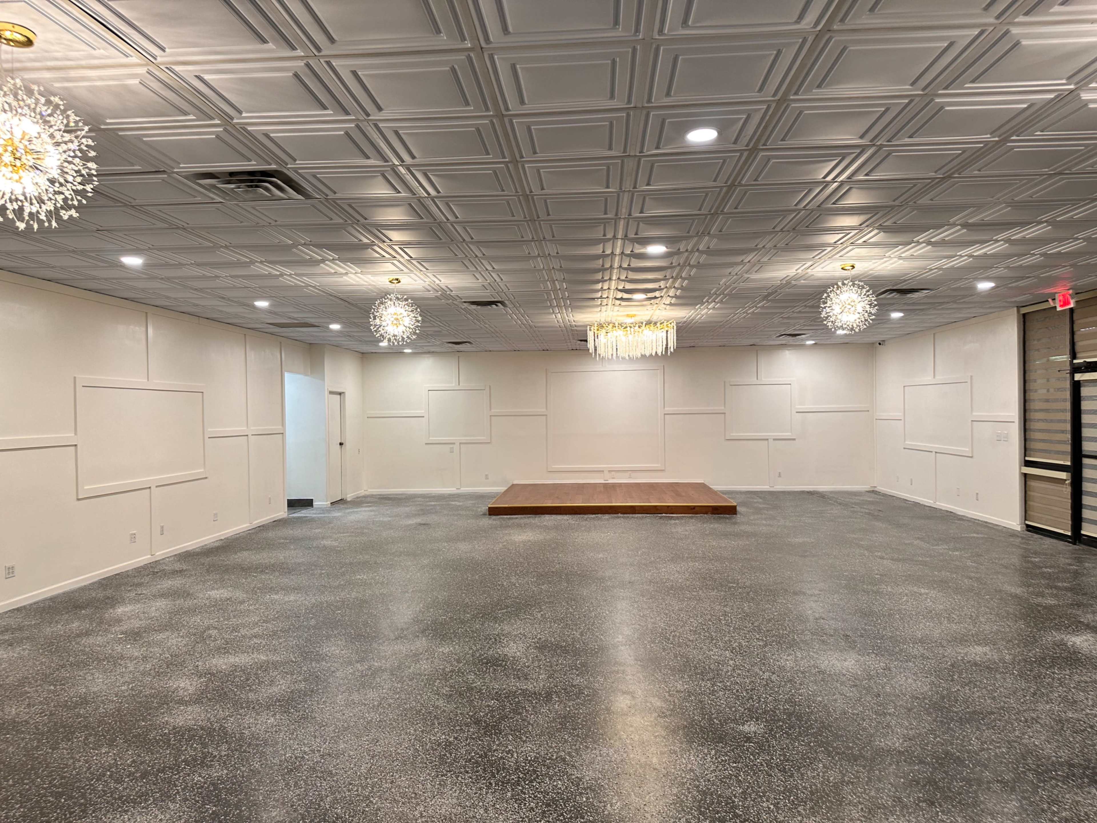 A spacious, empty interior room with a wooden stage and decorative ceiling lights.