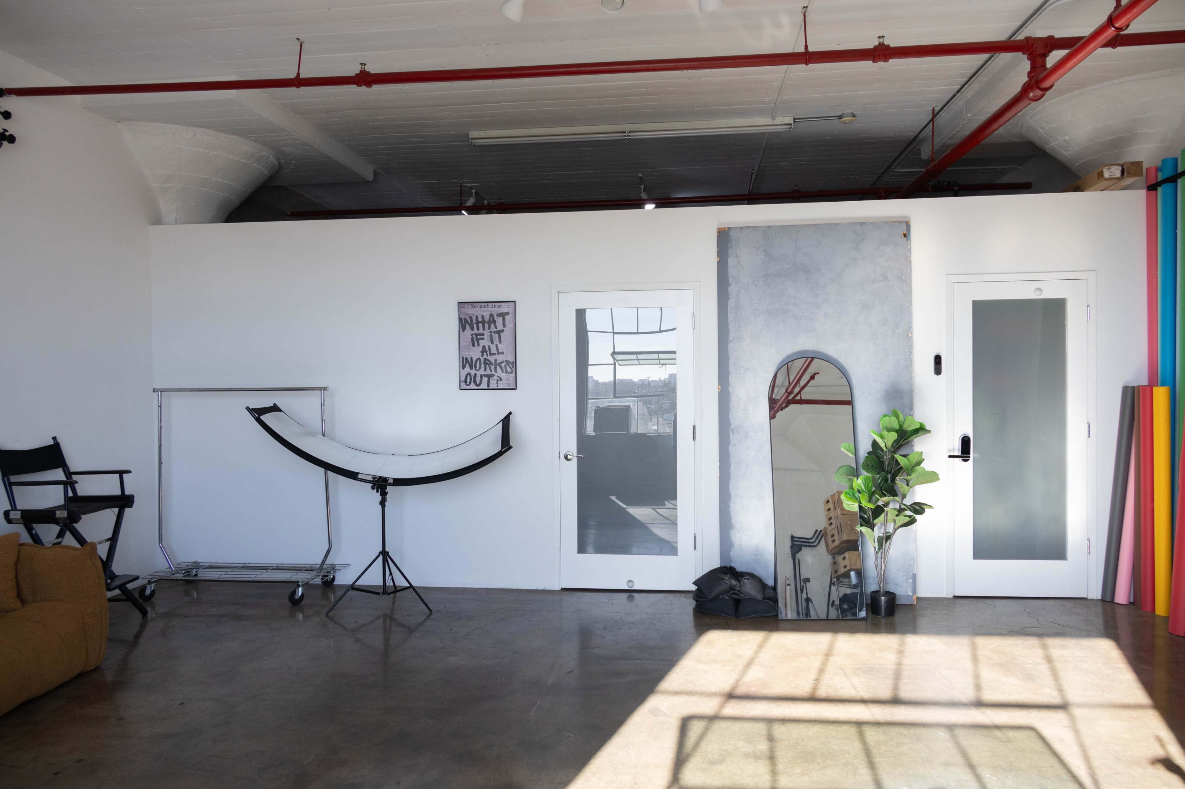 The image shows a spacious, brightly lit studio with a large mirror, a folding chair, and colorful backdrop panels leaning against the wall.