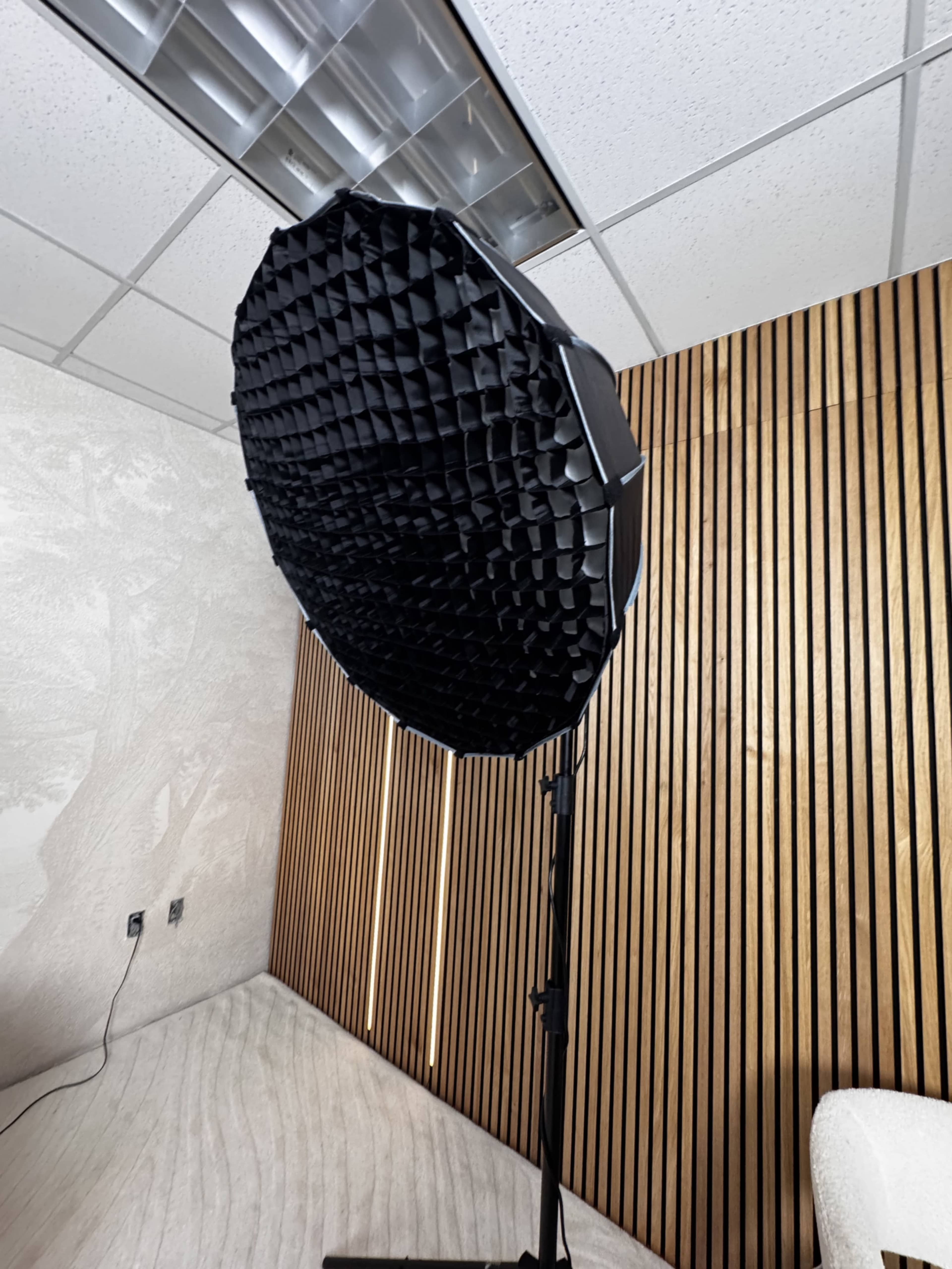 A large, octagonal softbox light is set up on a tripod in a modern room with wooden paneling and a light-colored floor.