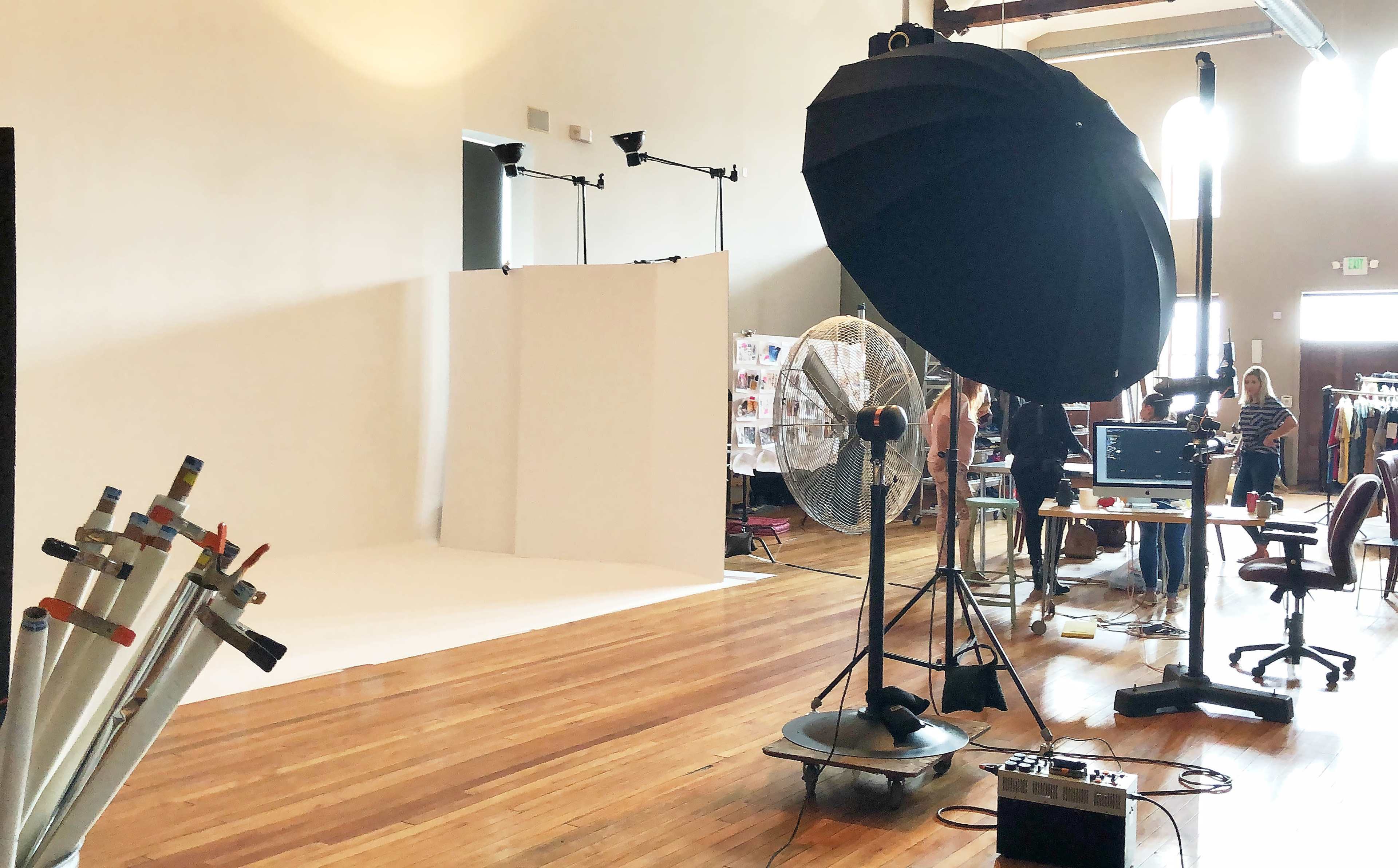 A photography studio with a white backdrop, lighting equipment, and various props arranged in a spacious room featuring wooden floors.