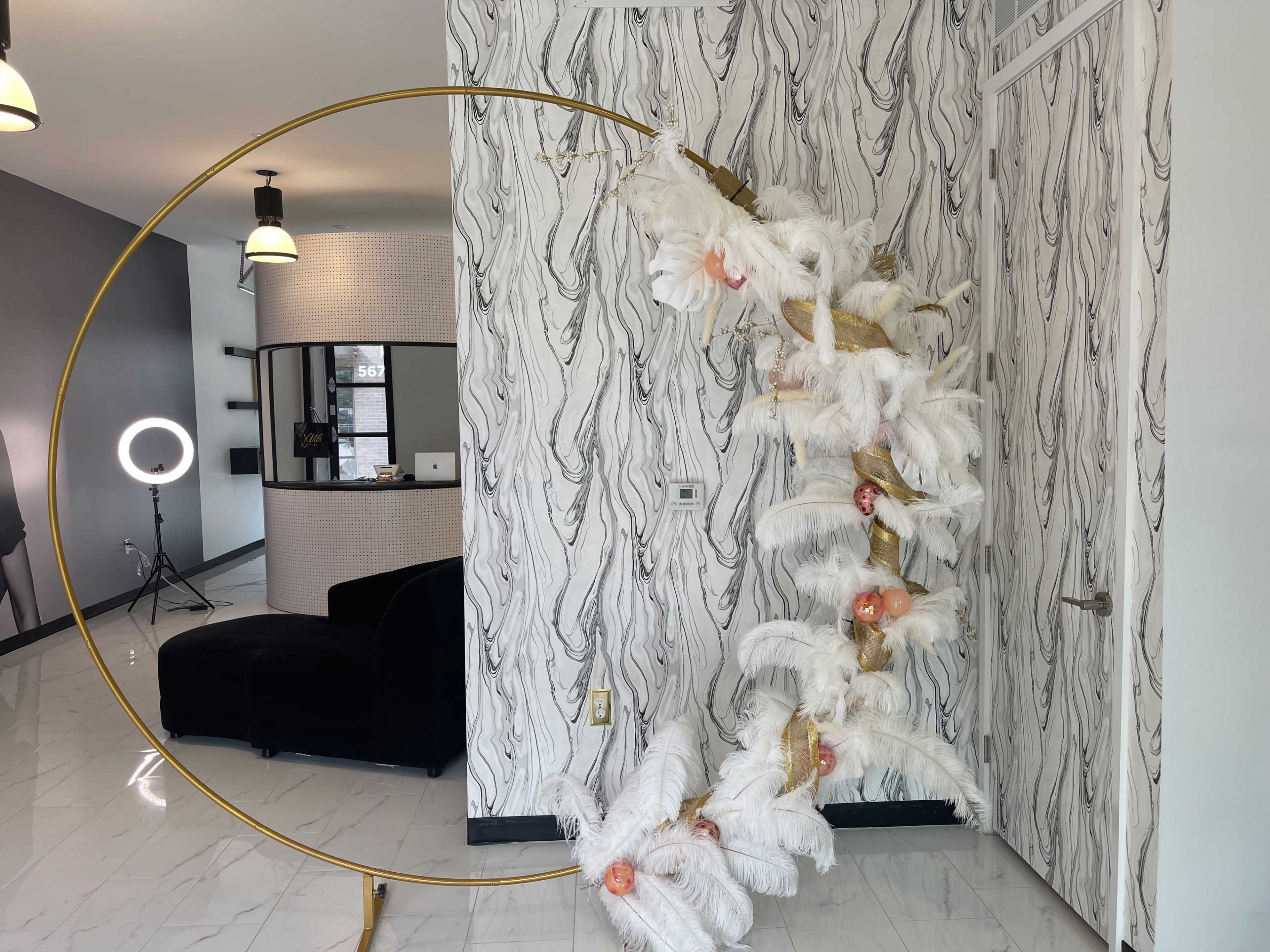 A tall decorative structure made of gold metal and white feathers is positioned near a reception area with a circular mirror and seating.