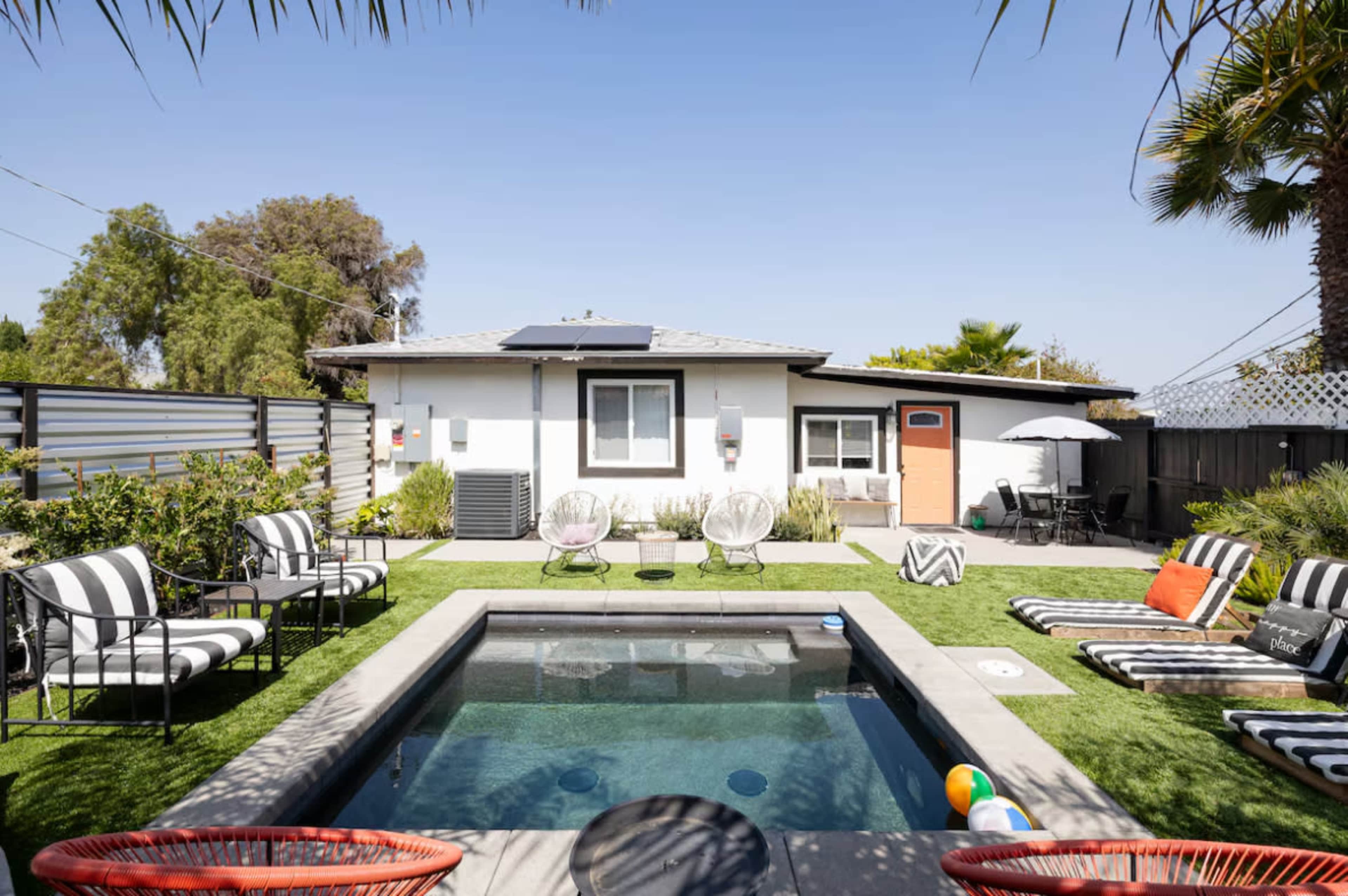 The image shows a backyard with a small pool surrounded by lounge chairs and a house in the background.