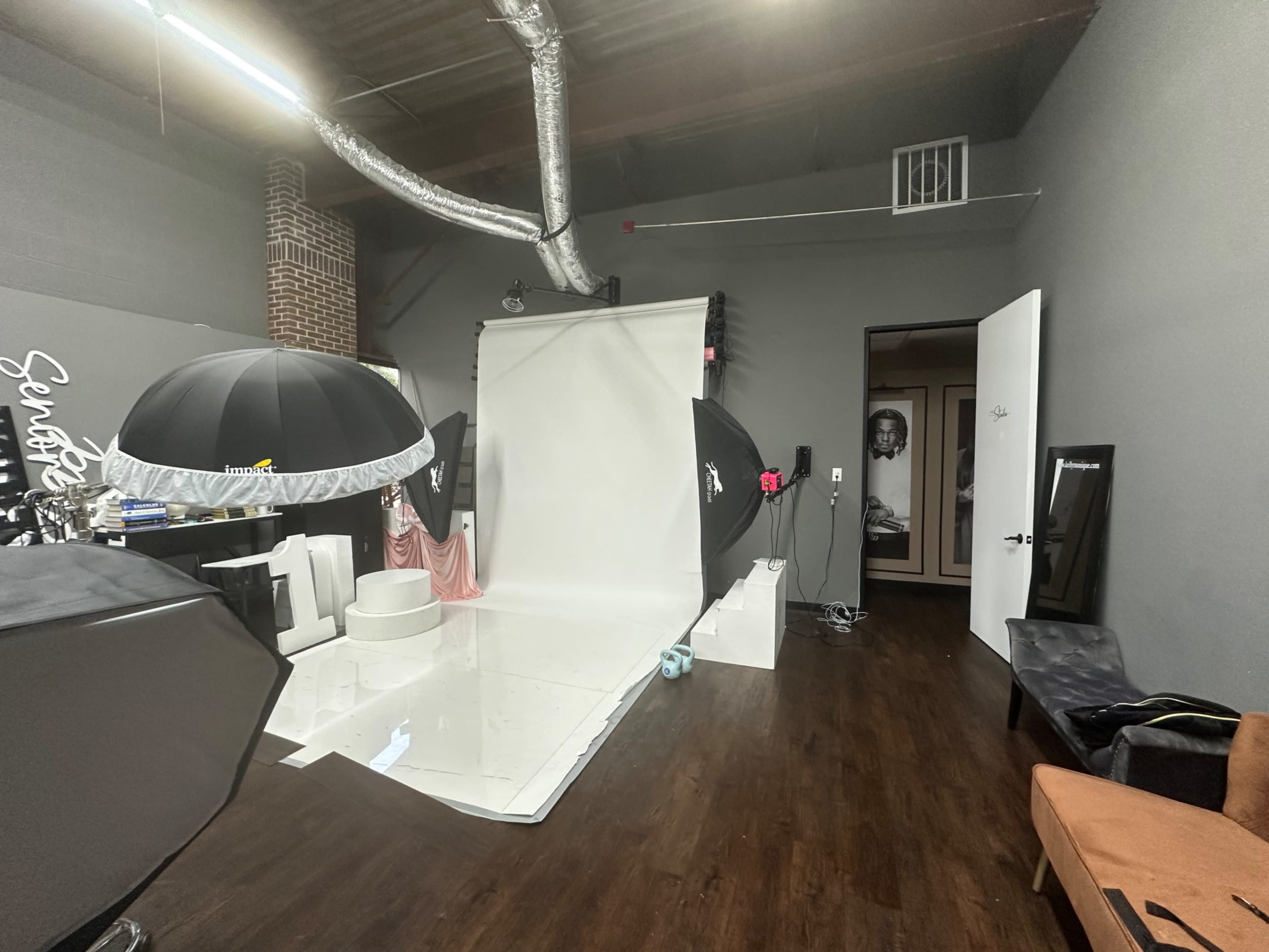 The image shows a photography studio with a white backdrop, lighting equipment, and a door leading to another room.
