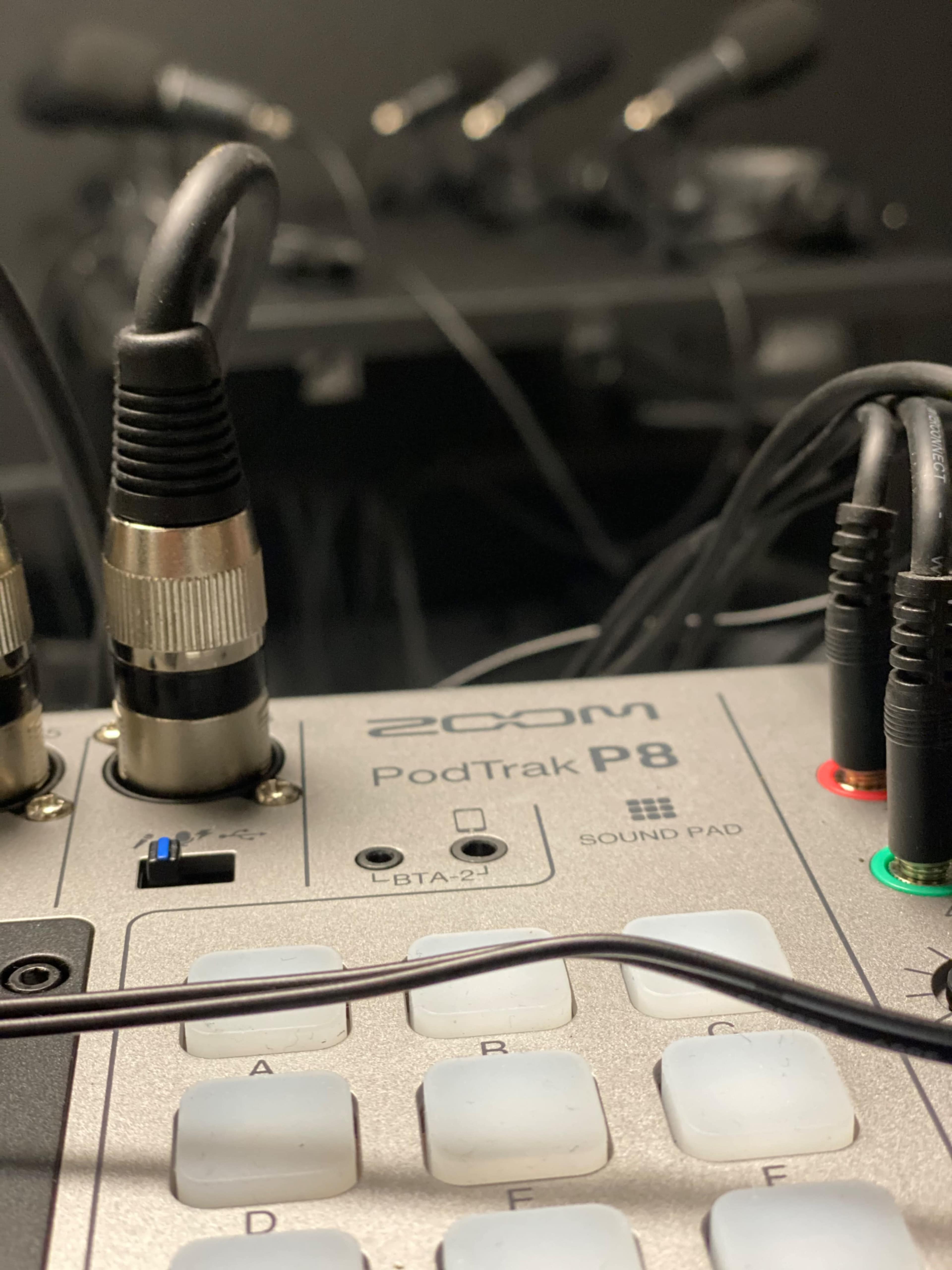 A close-up of a Zoom PodTrak P8 audio mixer with various input and output cables connected.