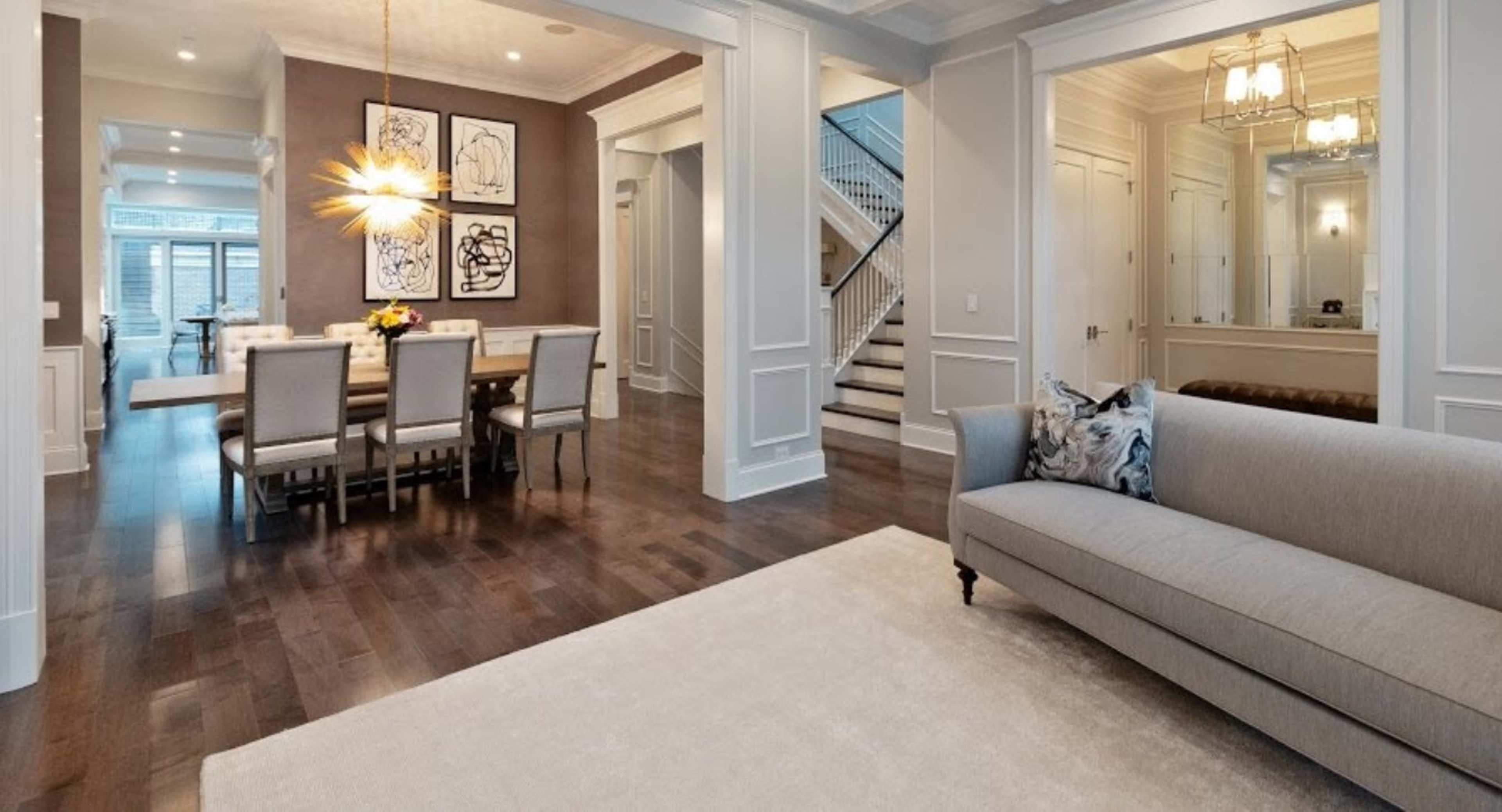 A modern open-concept living area with a sofa, a dining table set for eight, and a staircase in the background.