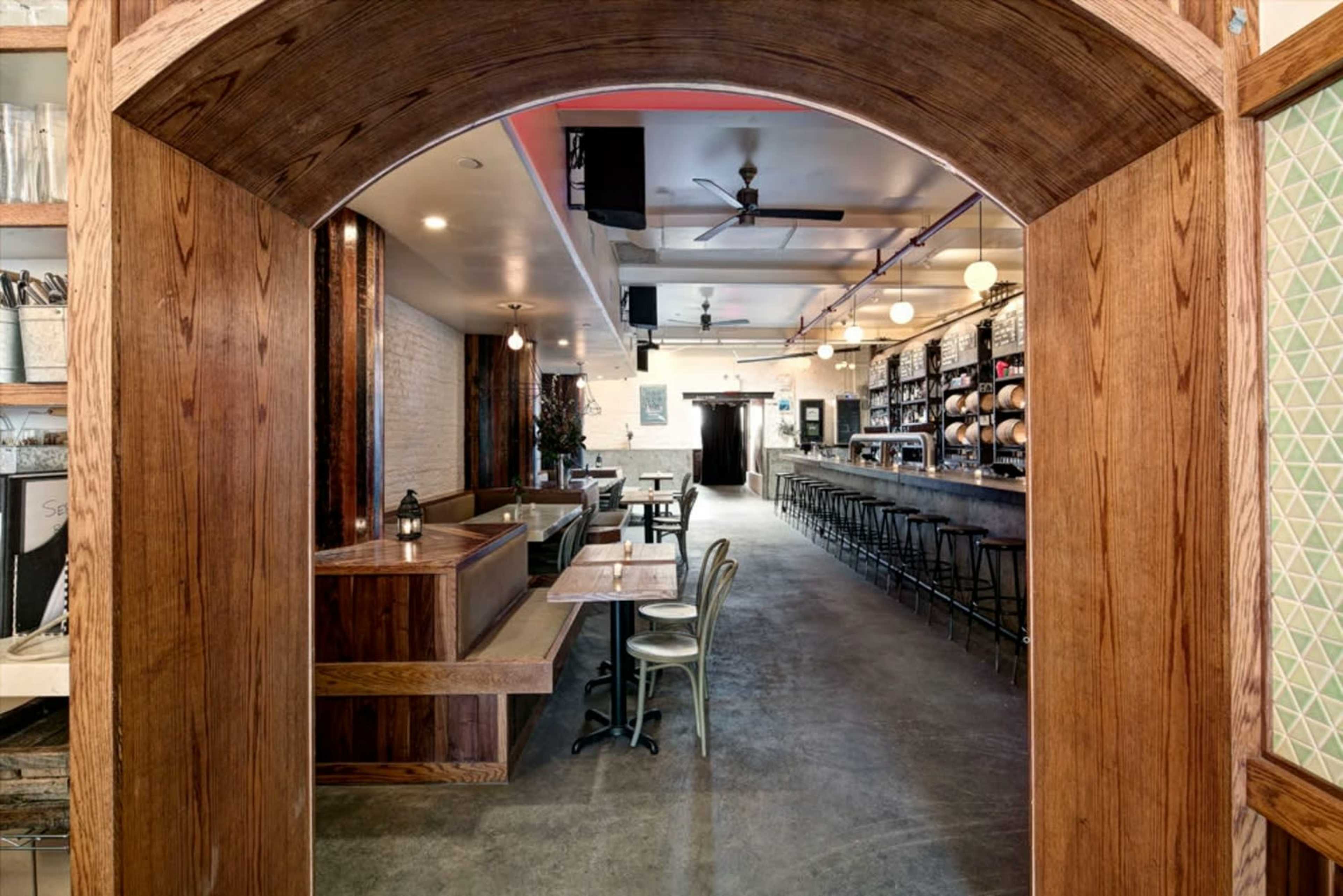 The image shows the interior of a restaurant, featuring wooden elements, bar seating, and various tables arranged throughout the space.