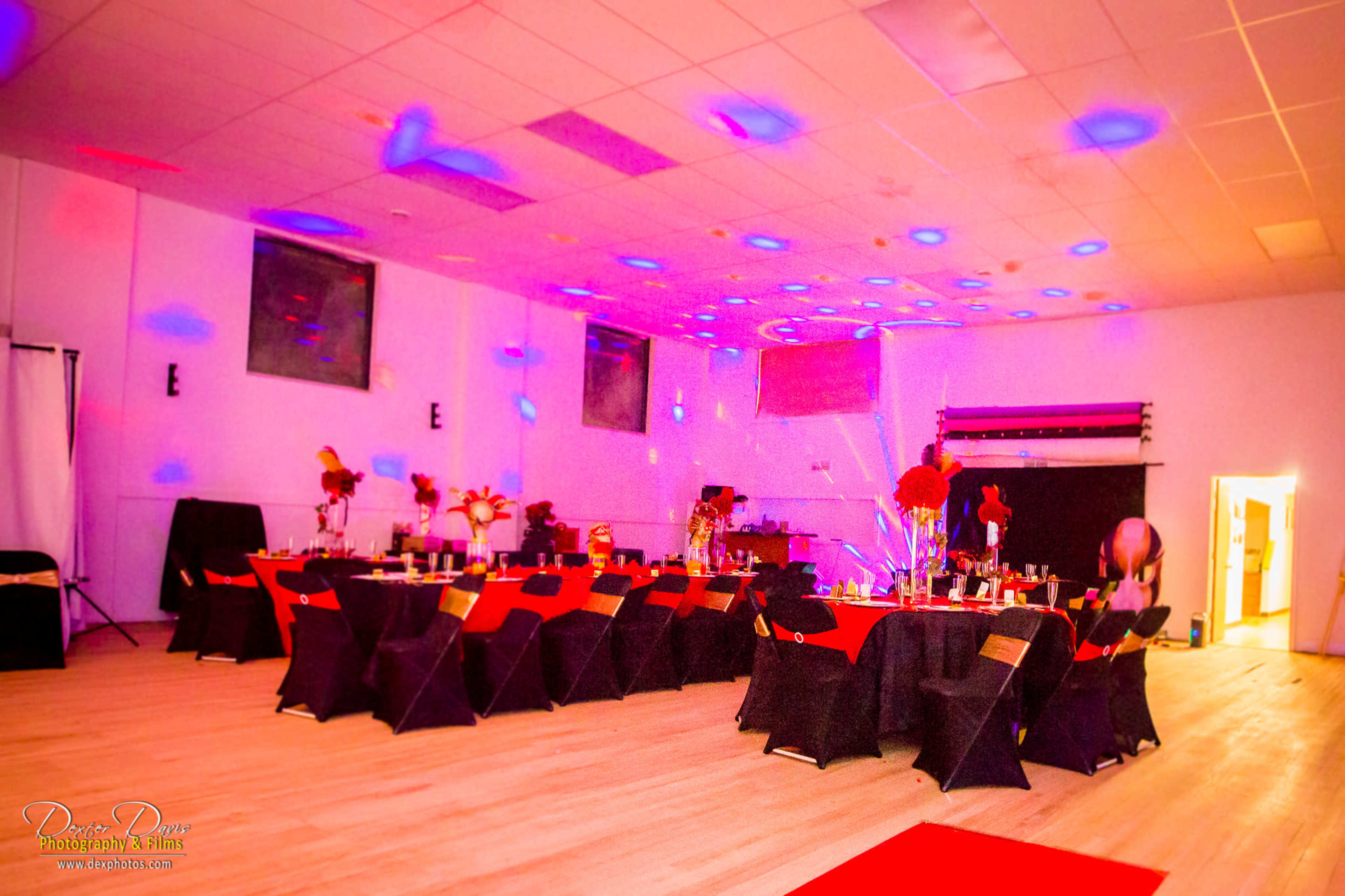 A banquet hall set up for an event, featuring tables decorated with red and black tablecloths, flowers, and ambient lighting.