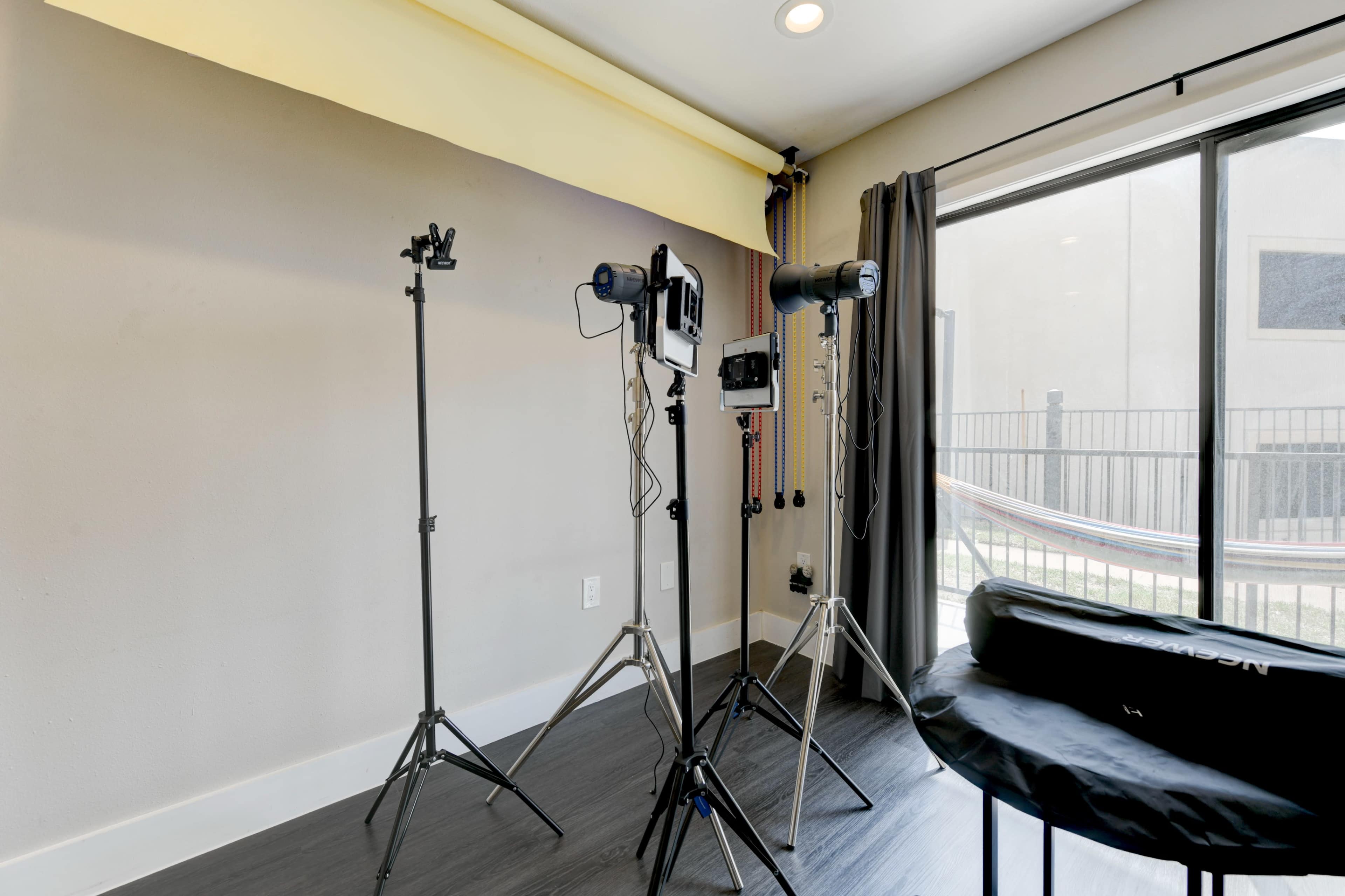 The image shows a room with two light stands and a camera mounted on a tripod, positioned near a large window with a view of an outdoor hammock.