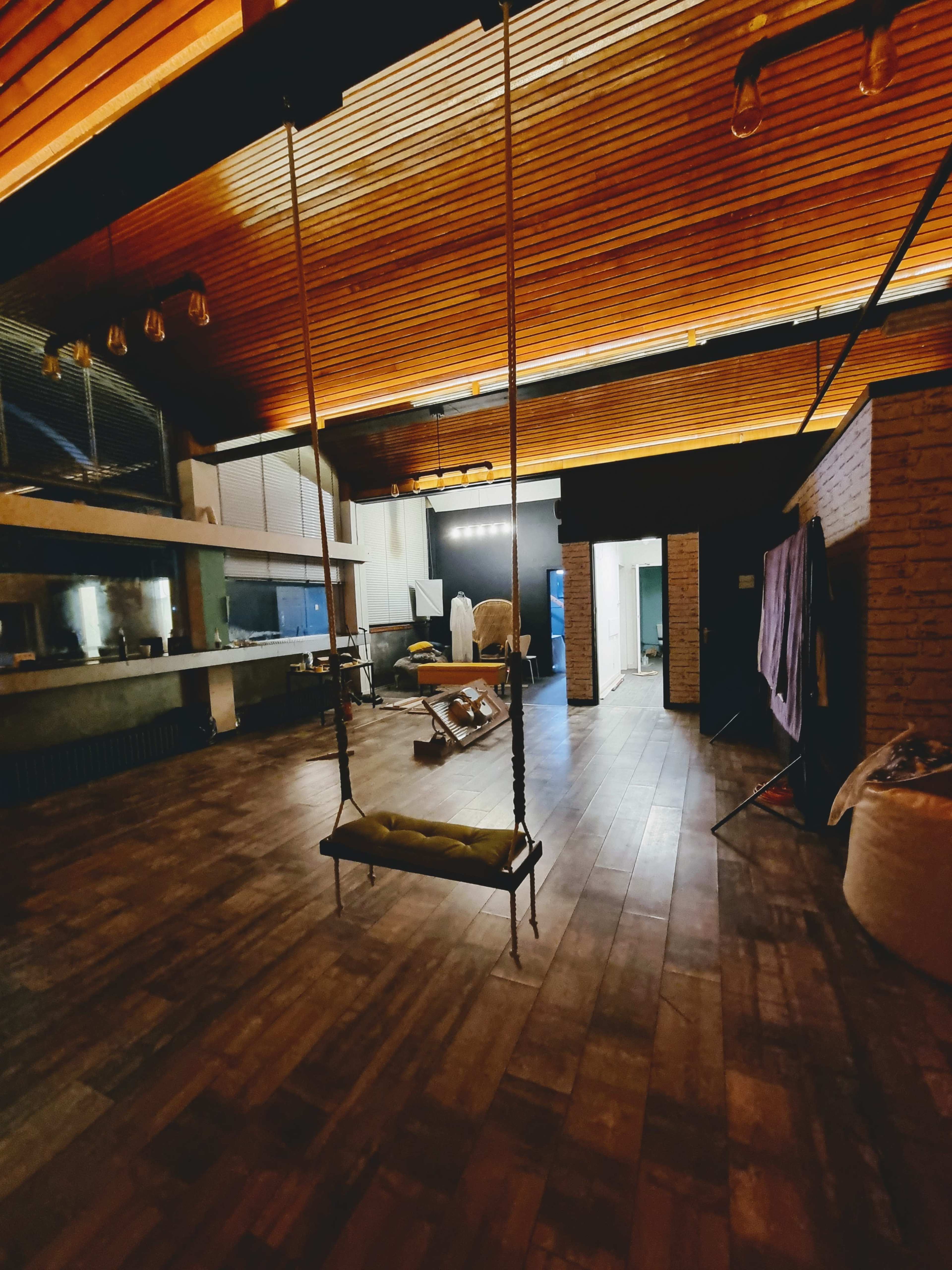 A spacious, modern interior with wooden ceilings, a swing hanging from the ceiling, and various furniture items scattered throughout the room.