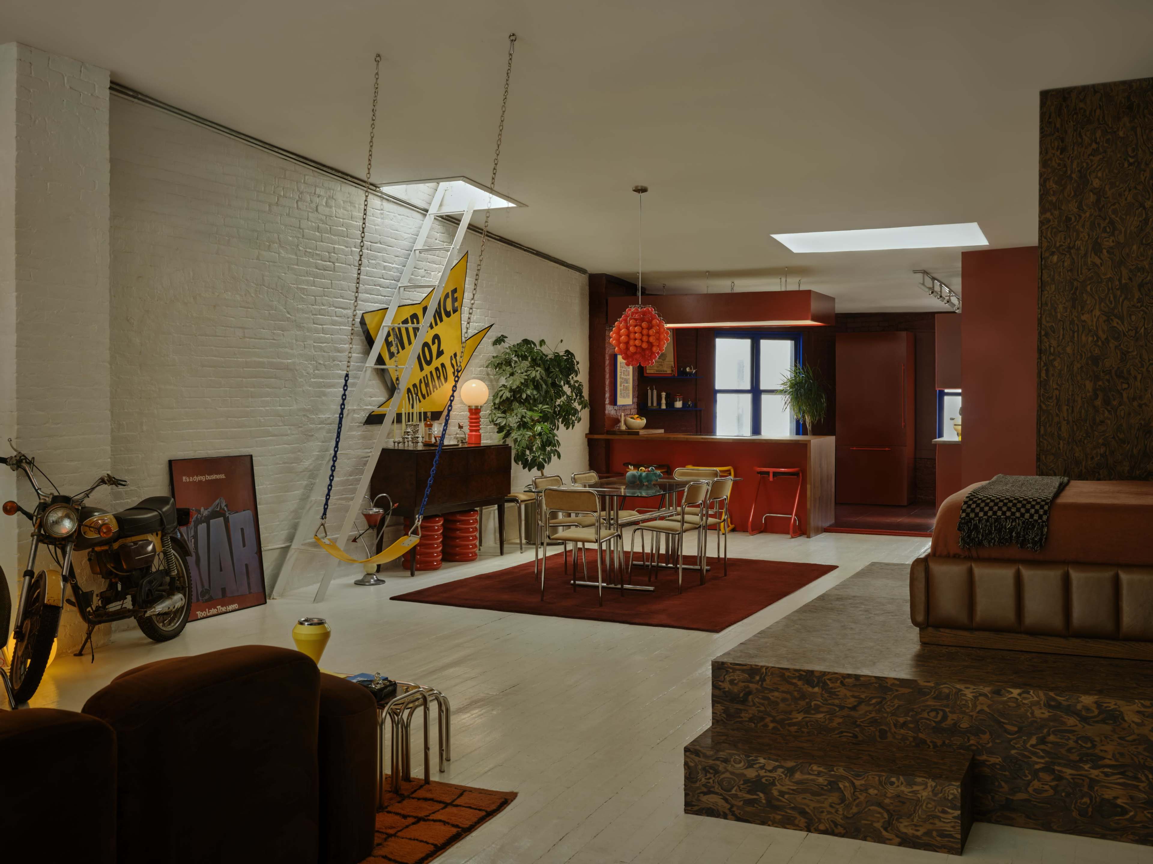 The image shows a modern open-plan apartment with a spacious living area, dining space, and a kitchen featuring colorful decor and furniture.