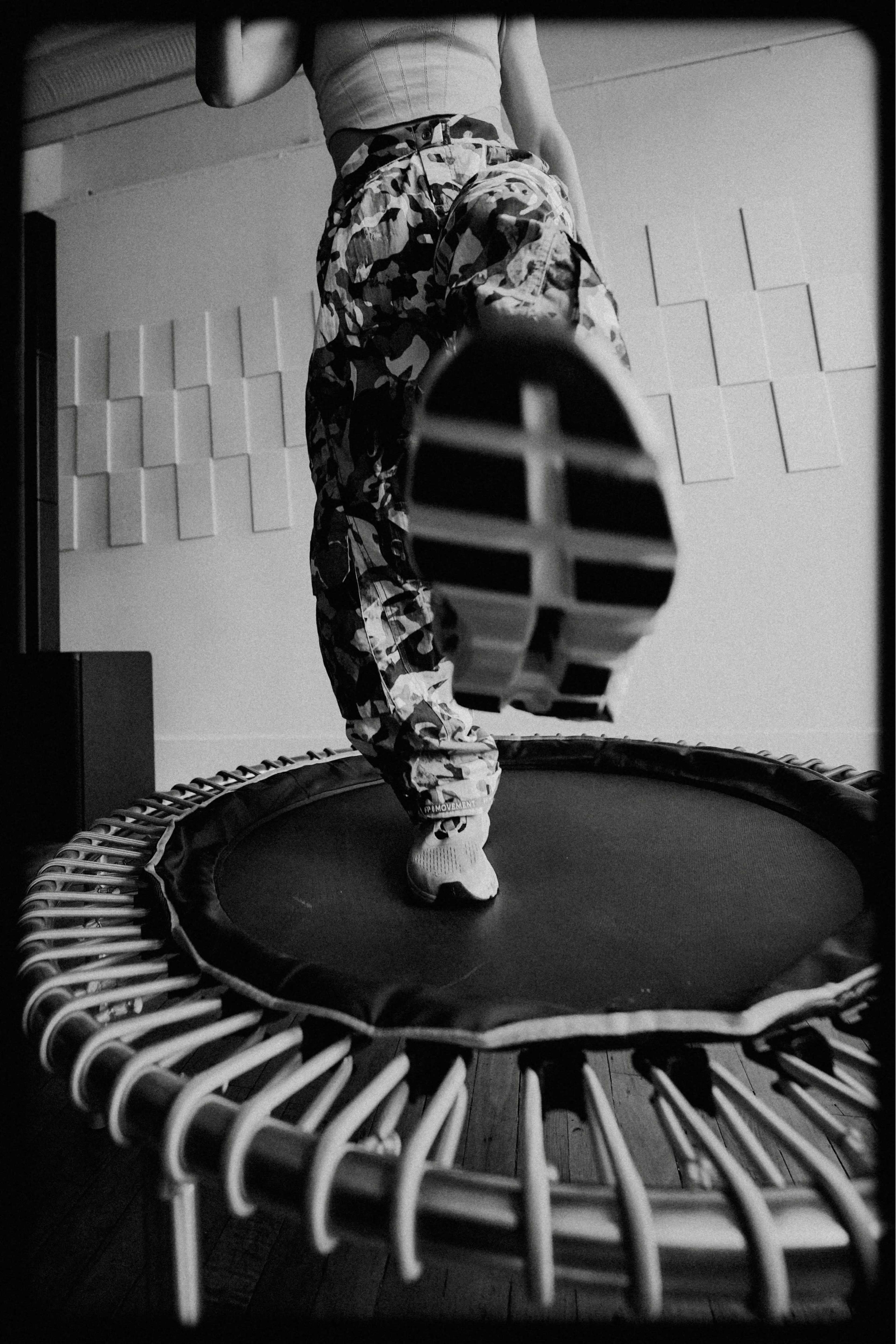 A person wearing camouflage pants is stepping onto a trampoline.