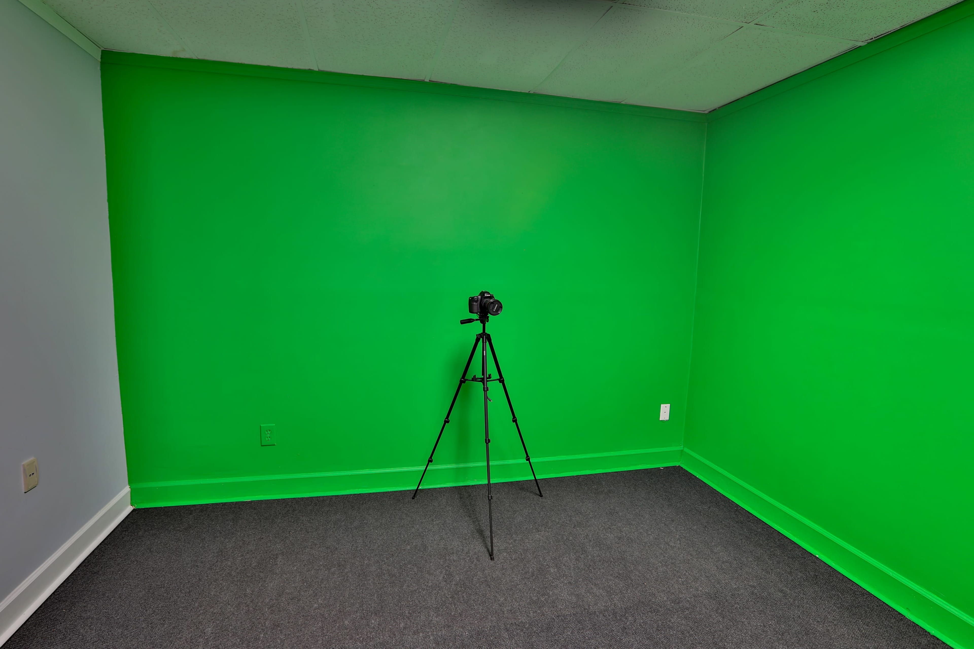 A room with a bright green wall, featuring a camera mounted on a tripod in the center.