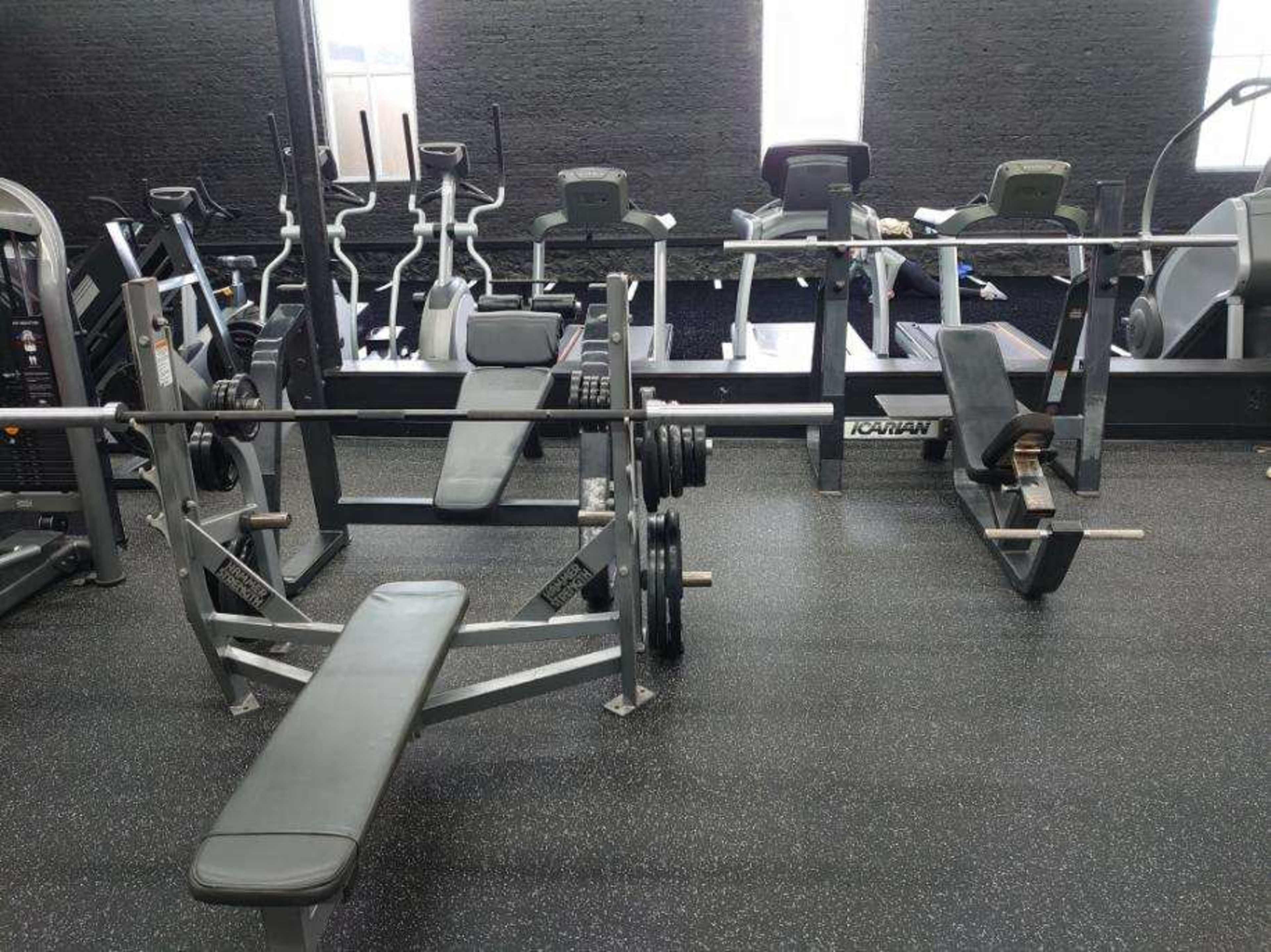 The image shows a gym interior with several pieces of workout equipment, including benches and exercise machines arranged neatly.