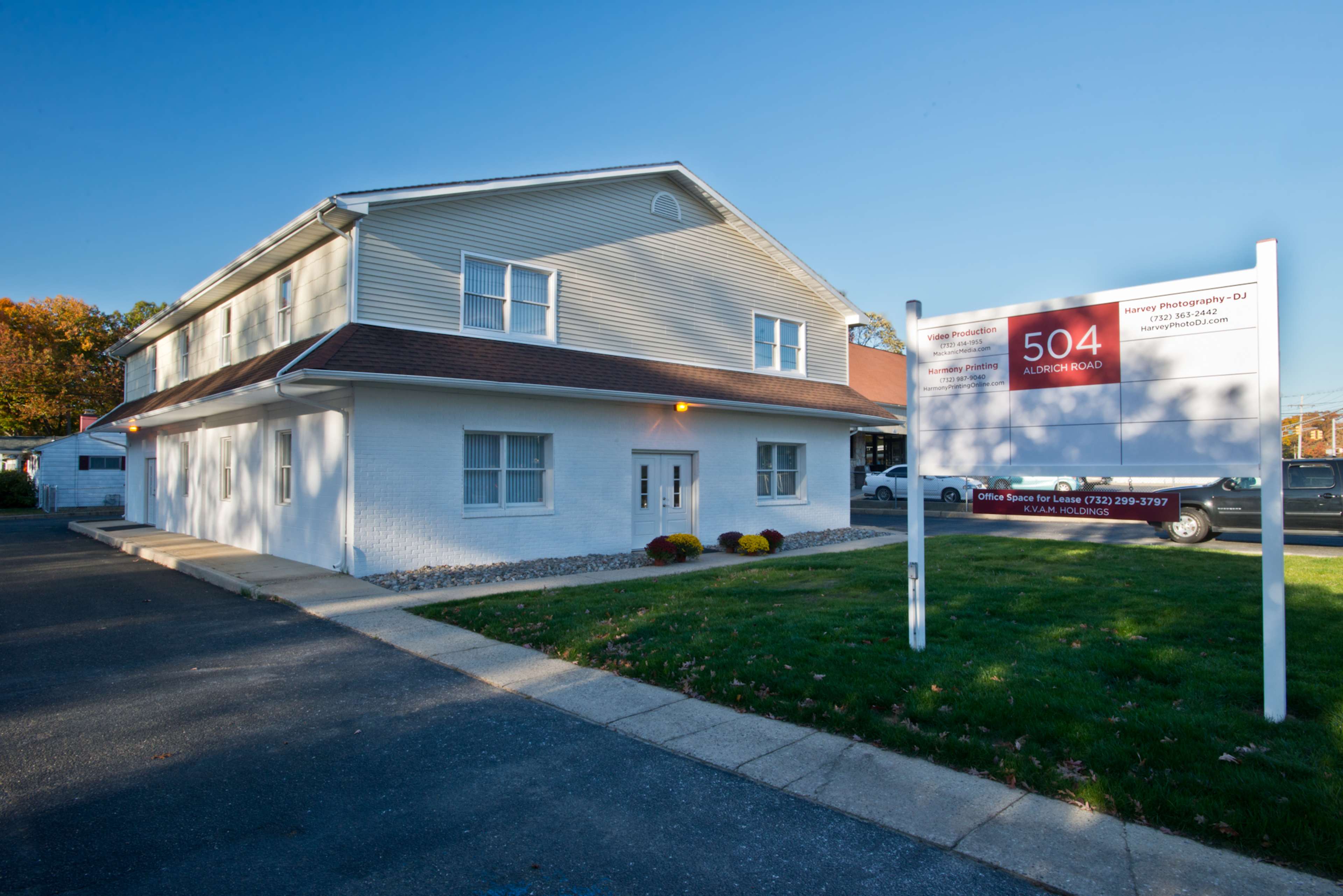 A two-story office building with a white exterior and a large sign displaying the address "504 Aldon Road" in front of it, surrounded by a small lawn and driveway.