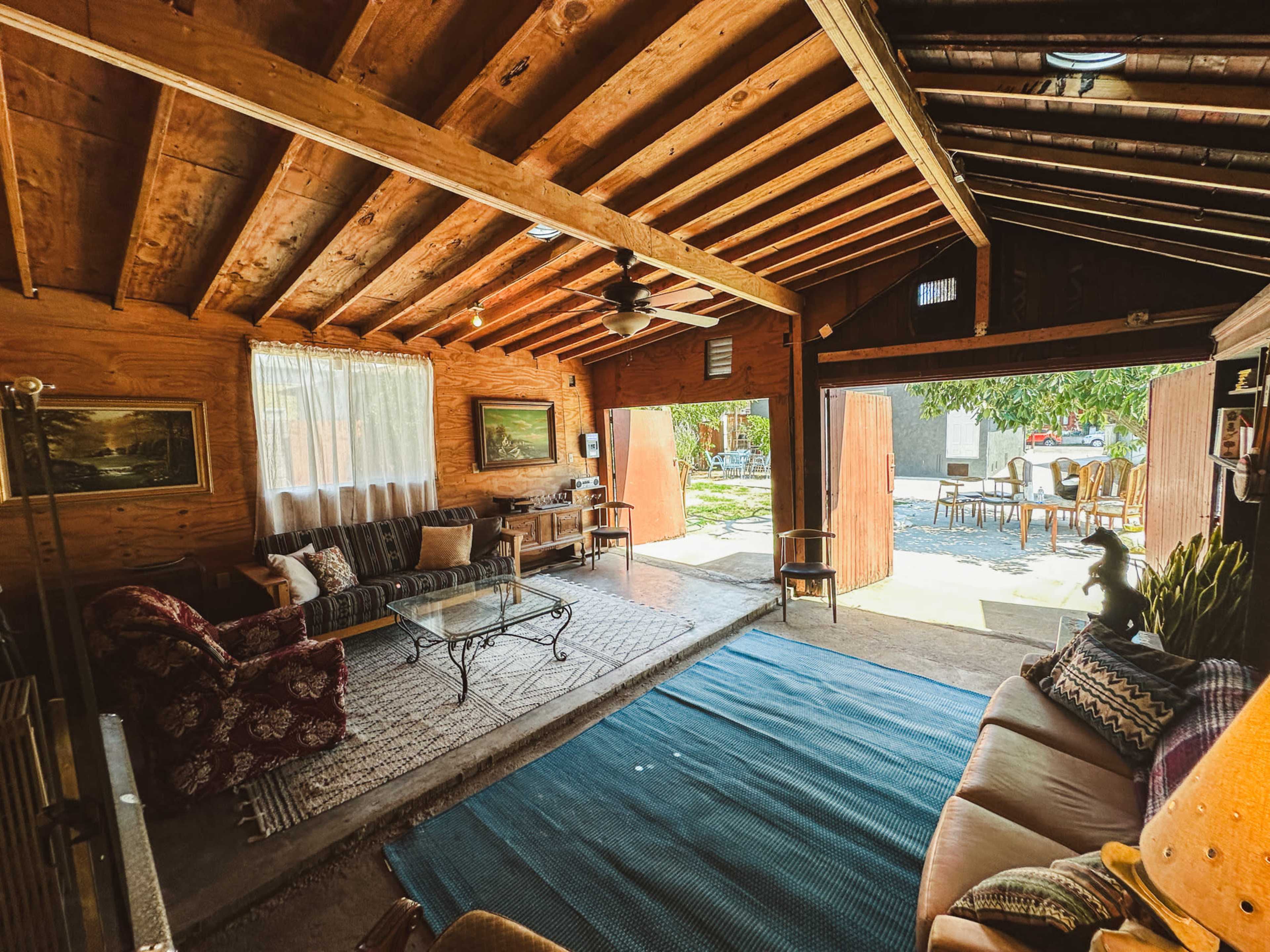 A rustic interior living space with wooden beams, comfortable seating, and a large opening leading to an outdoor area.