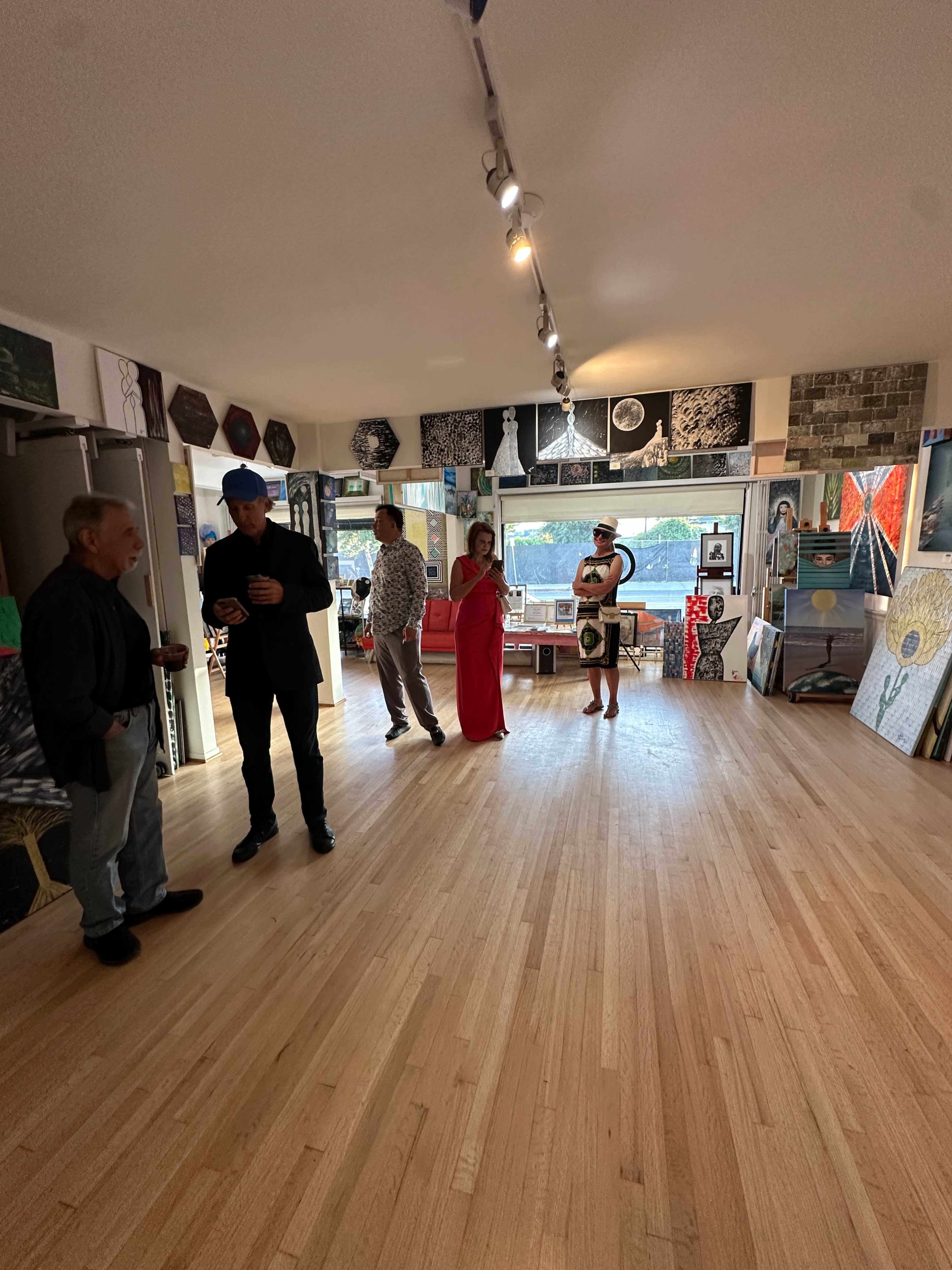 A group of people is socializing in an art gallery filled with various artworks displayed on the walls.