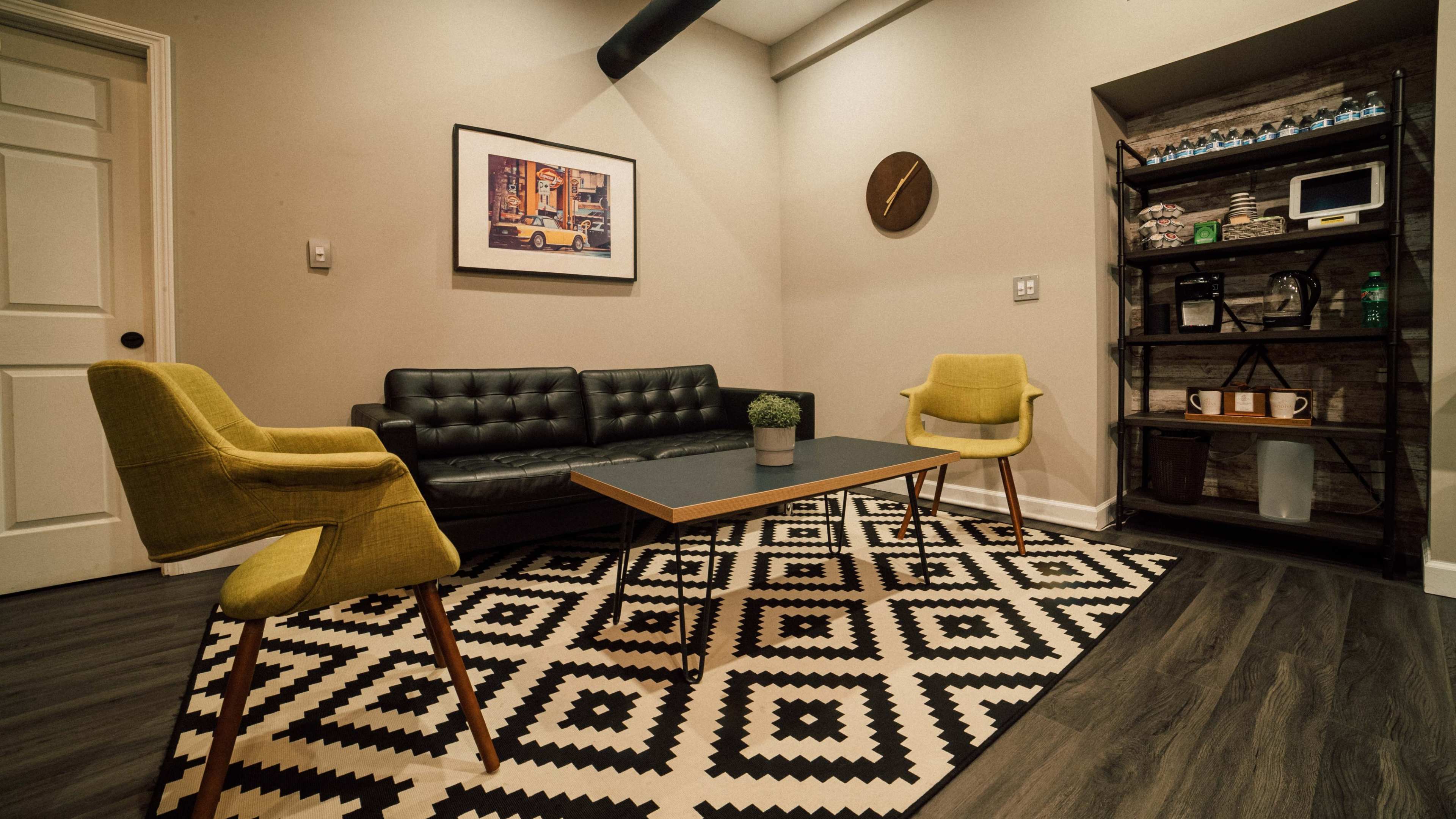 A compact modern sitting area with a black couch, two yellow chairs, a coffee table, and a patterned rug.