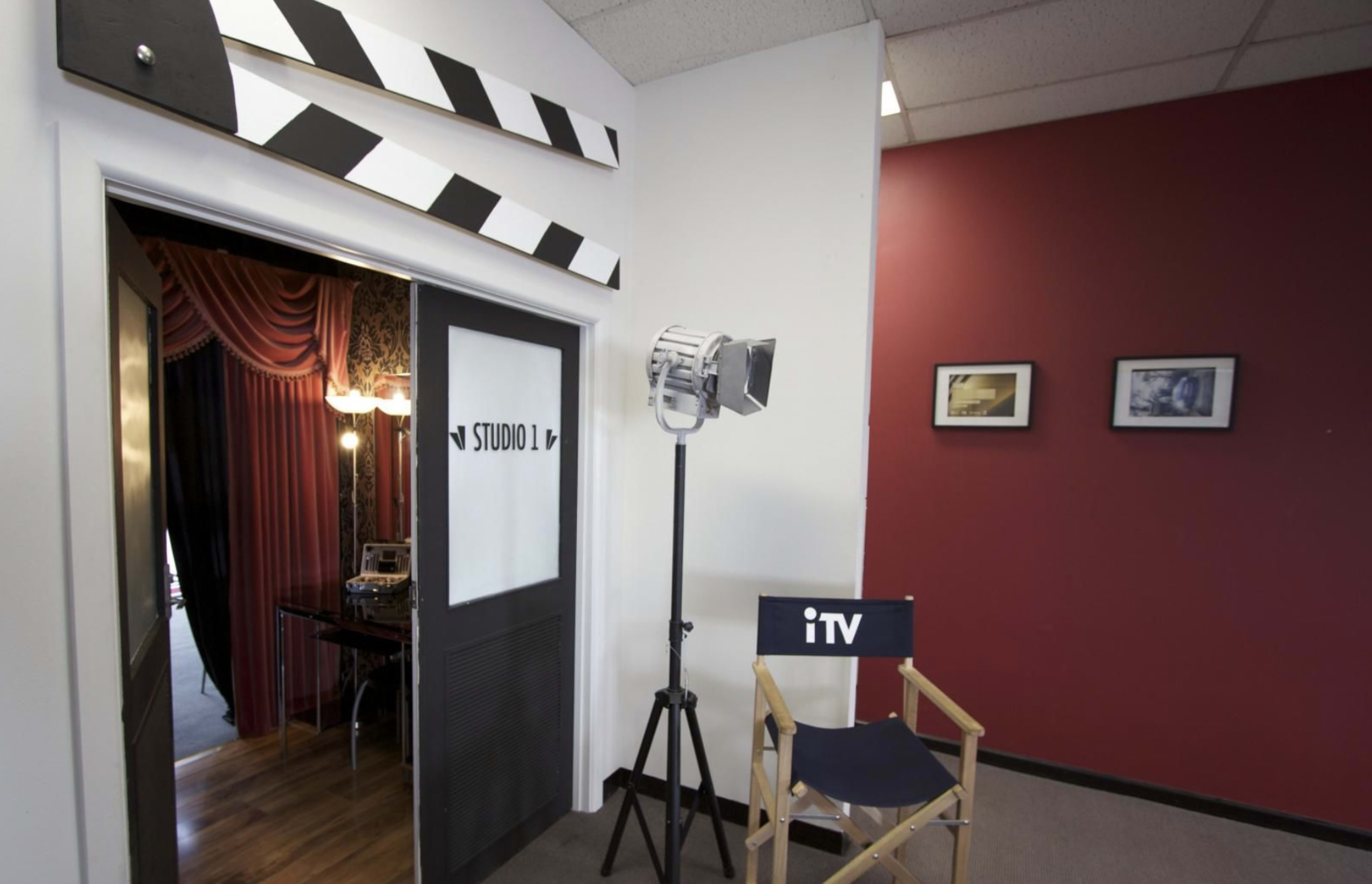 An entrance to a film studio labeled "STUDIO 1," featuring a director's clapboard above the door and a spotlight on a stand beside a director's chair.