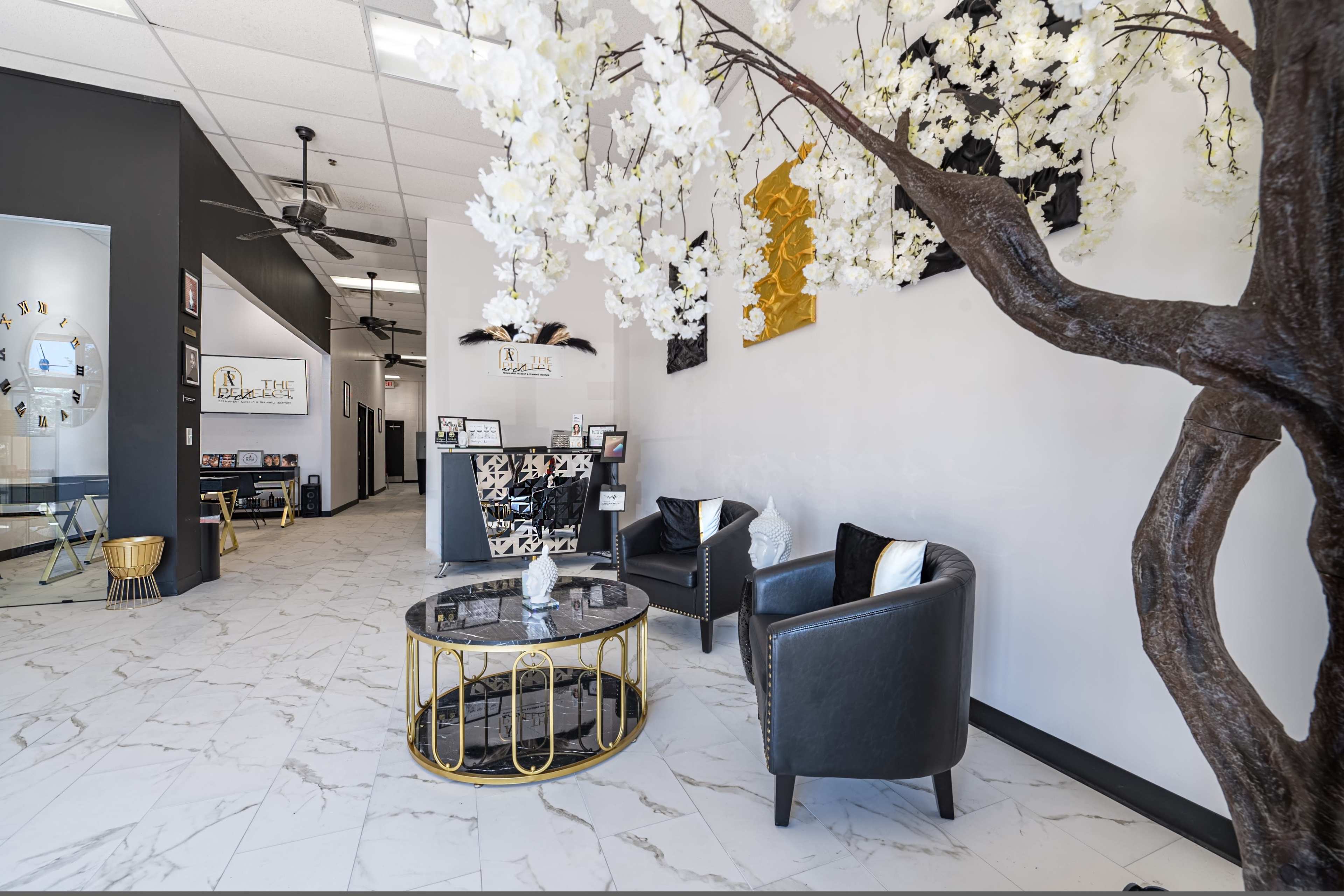 The image shows a modern reception area with a marble floor, black and white decor, and a large decorative tree with white flowers.