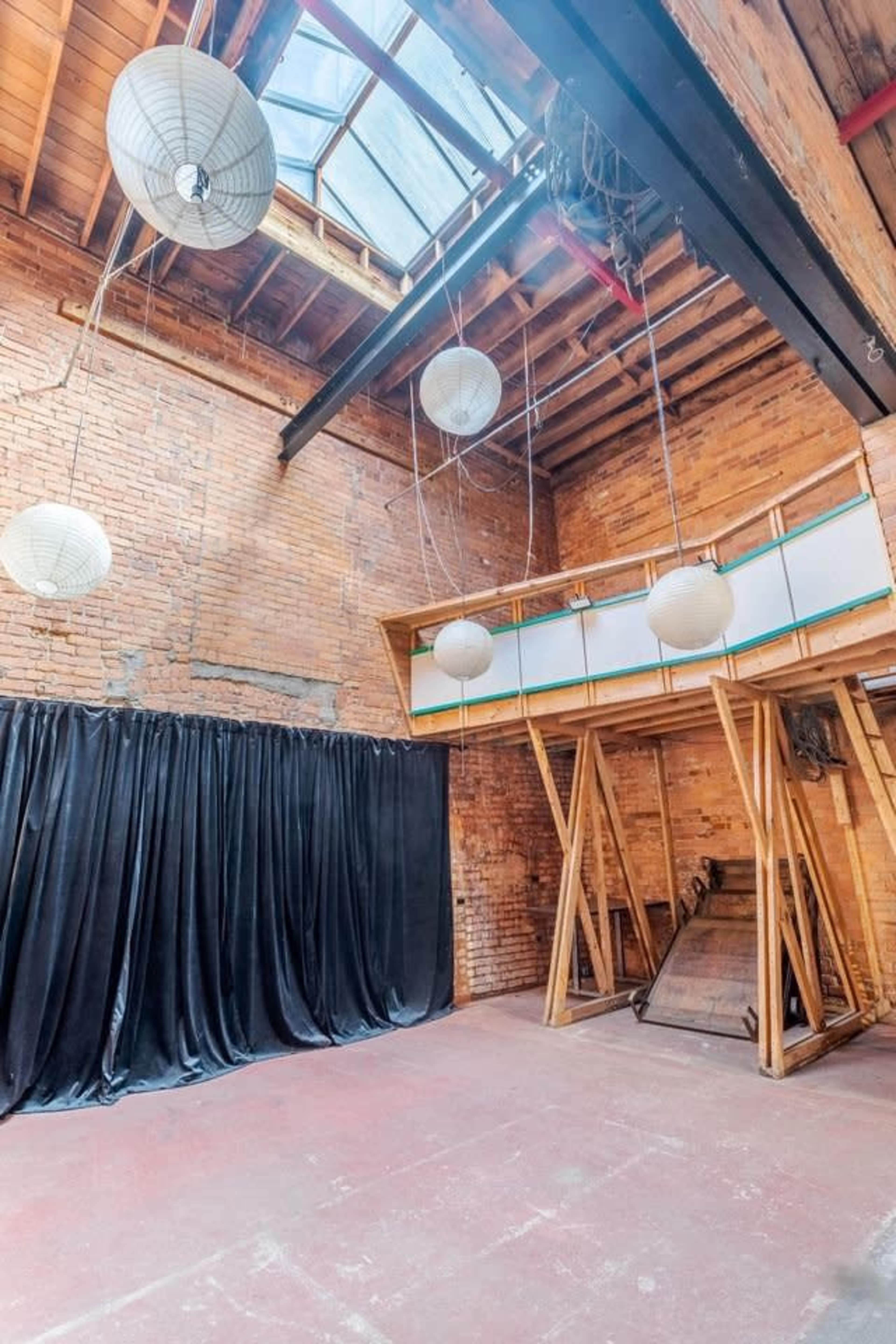 The image shows an industrial-style interior with exposed brick walls, a skylight, and hanging light fixtures.