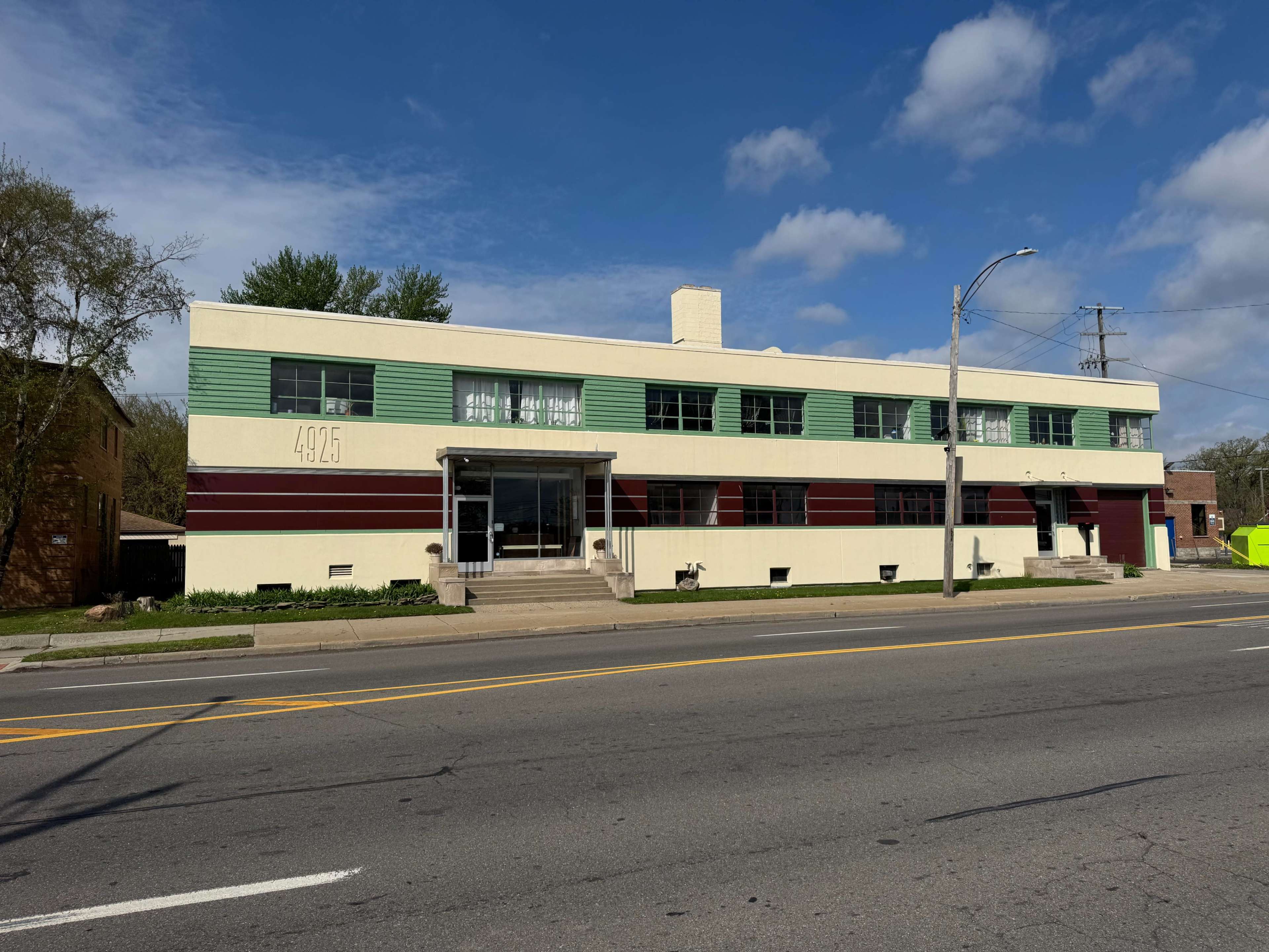 The image shows a two-story commercial building with a distinctive green and white facade, featuring large windows and decorative red bands.
