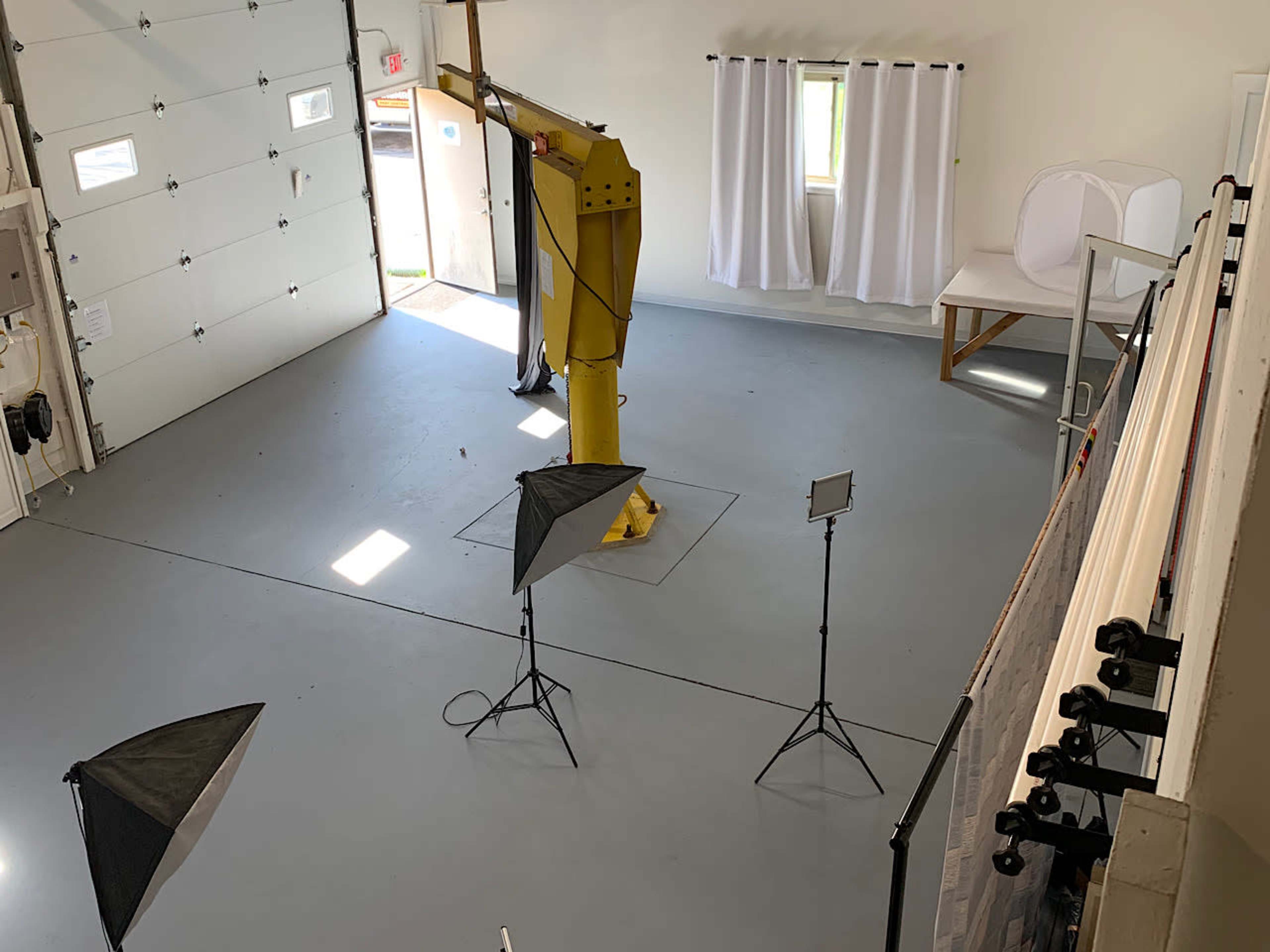 A spacious indoor studio with a yellow support structure in the center, multiple lighting setups, and a window draped with white curtains.