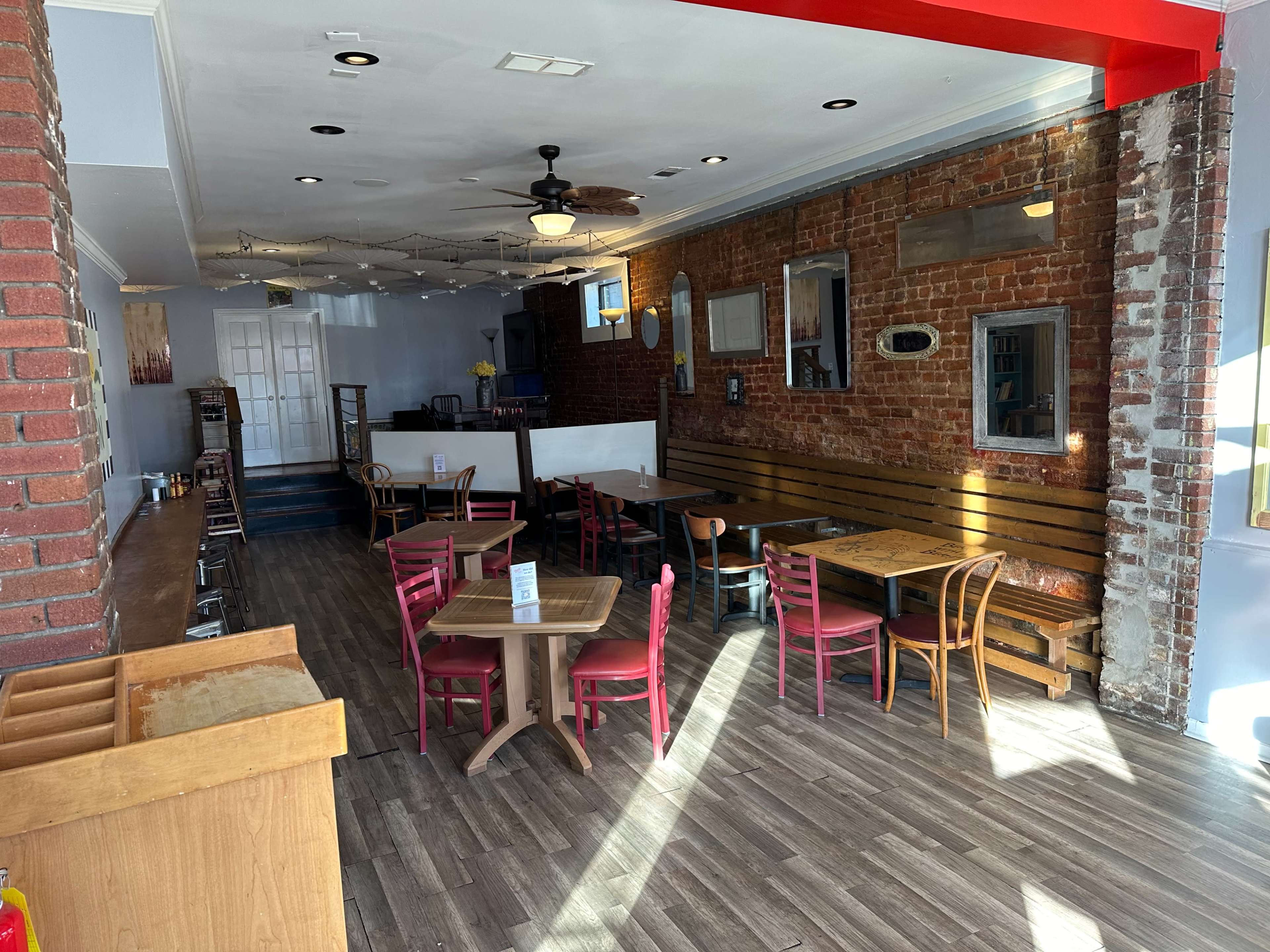 An interior of a rustic restaurant with wooden tables and chairs, brick walls, and a bright red ceiling.