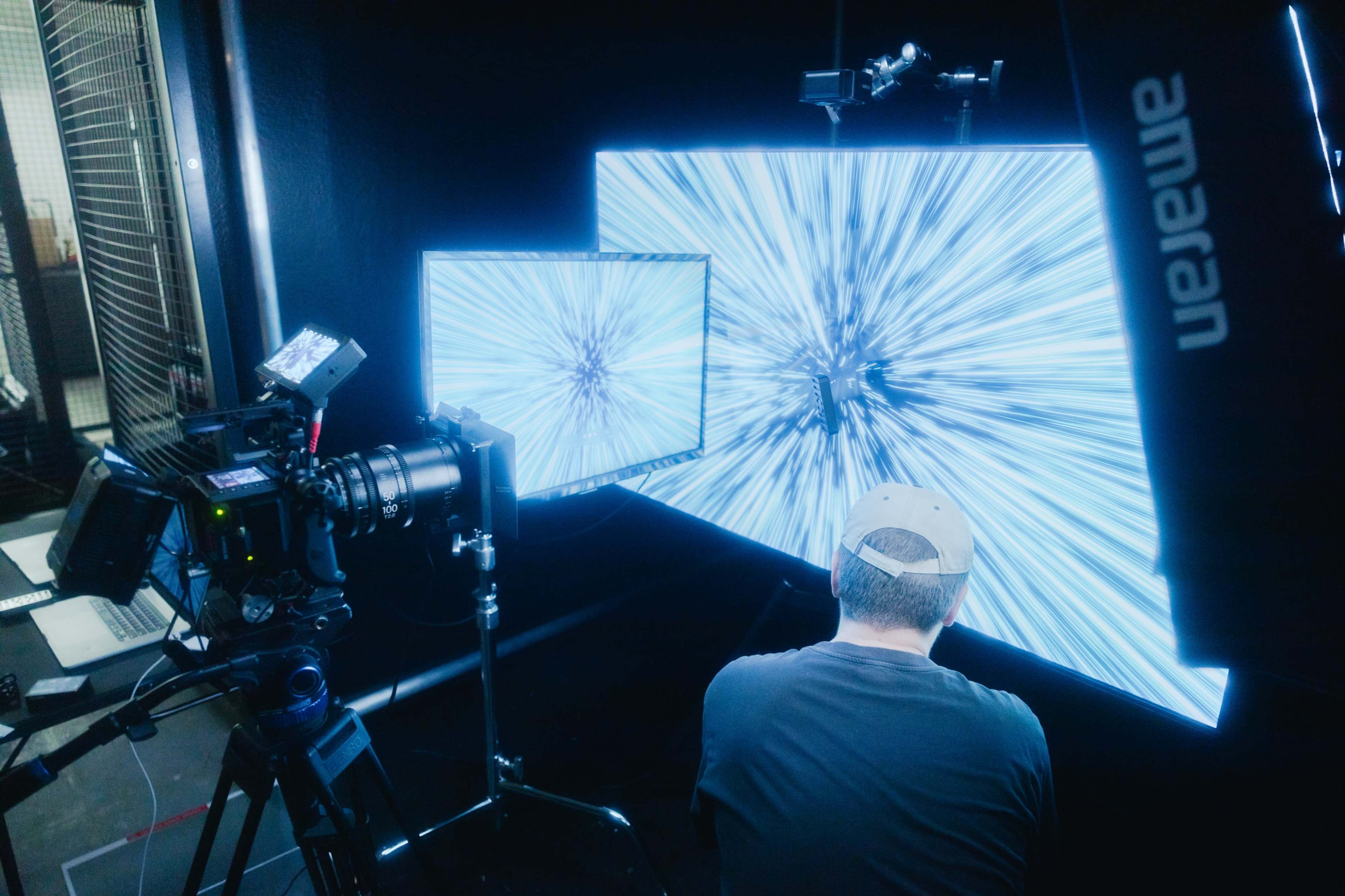 A person operates a camera while facing a large display that creates a visual effect of light streaks.