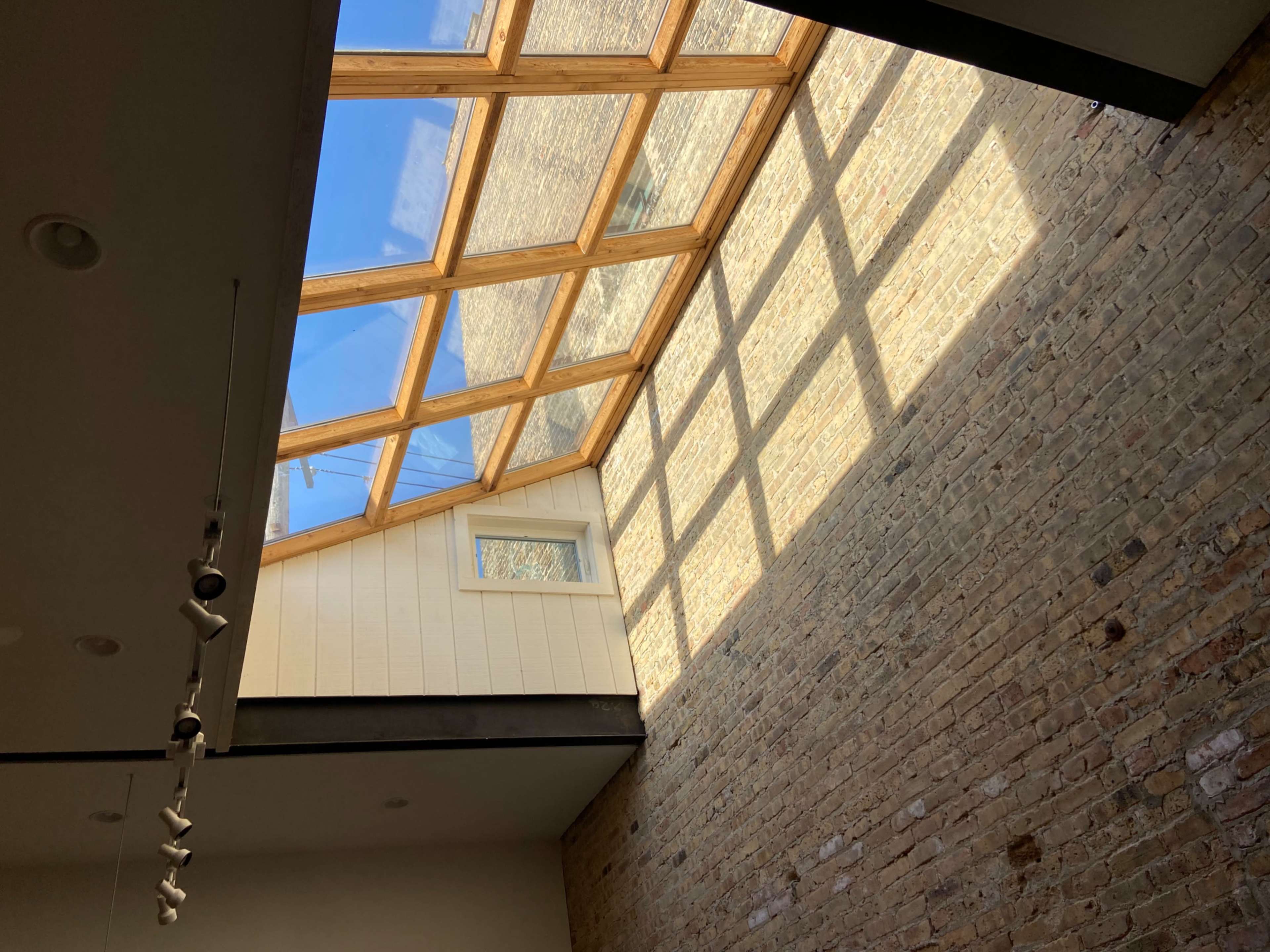 A skylight with wooden beams illuminates a room with a brick wall.