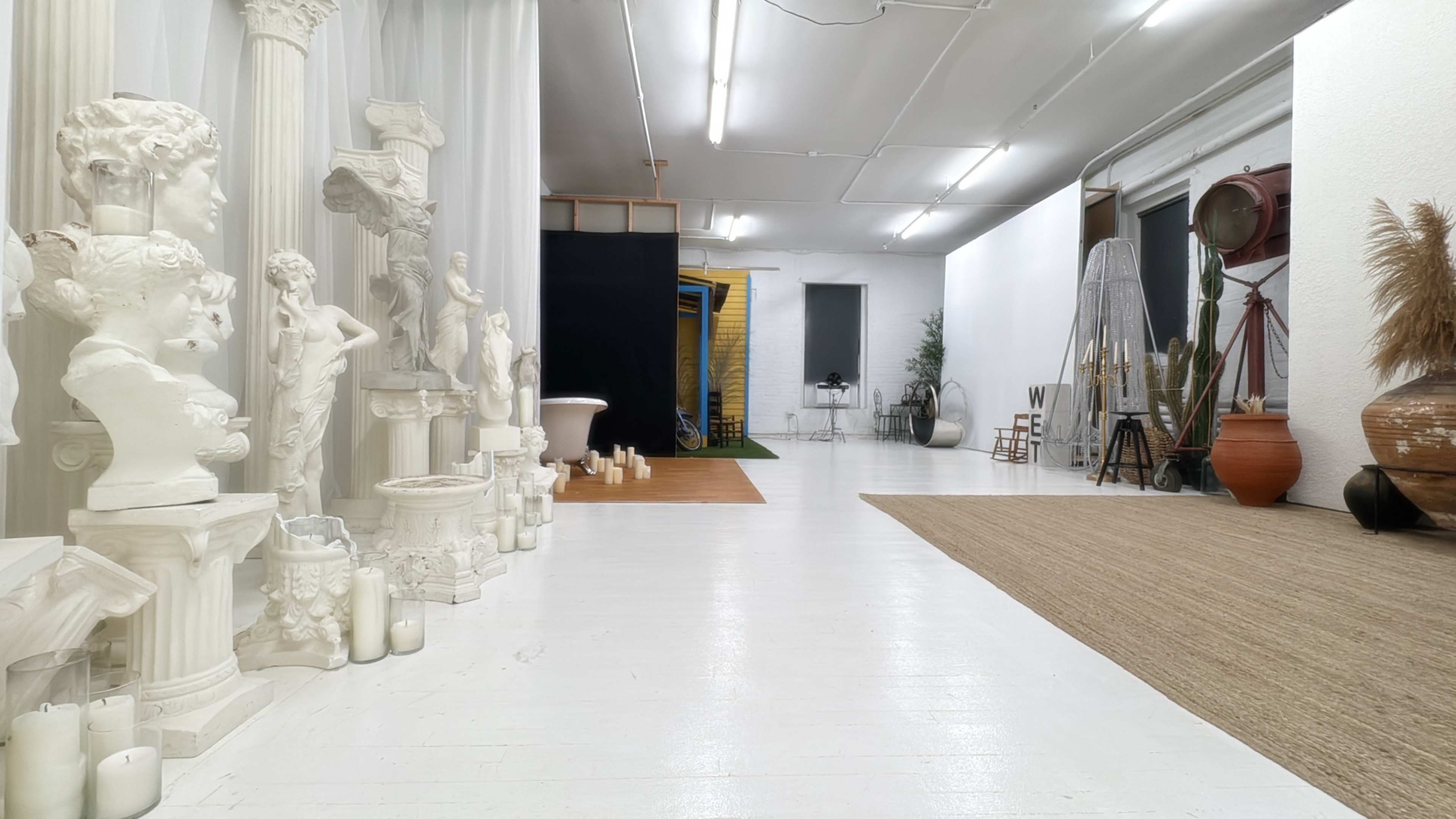 The image shows a spacious interior containing classical sculptures, soft lighting, and various decorative elements across a white floor.