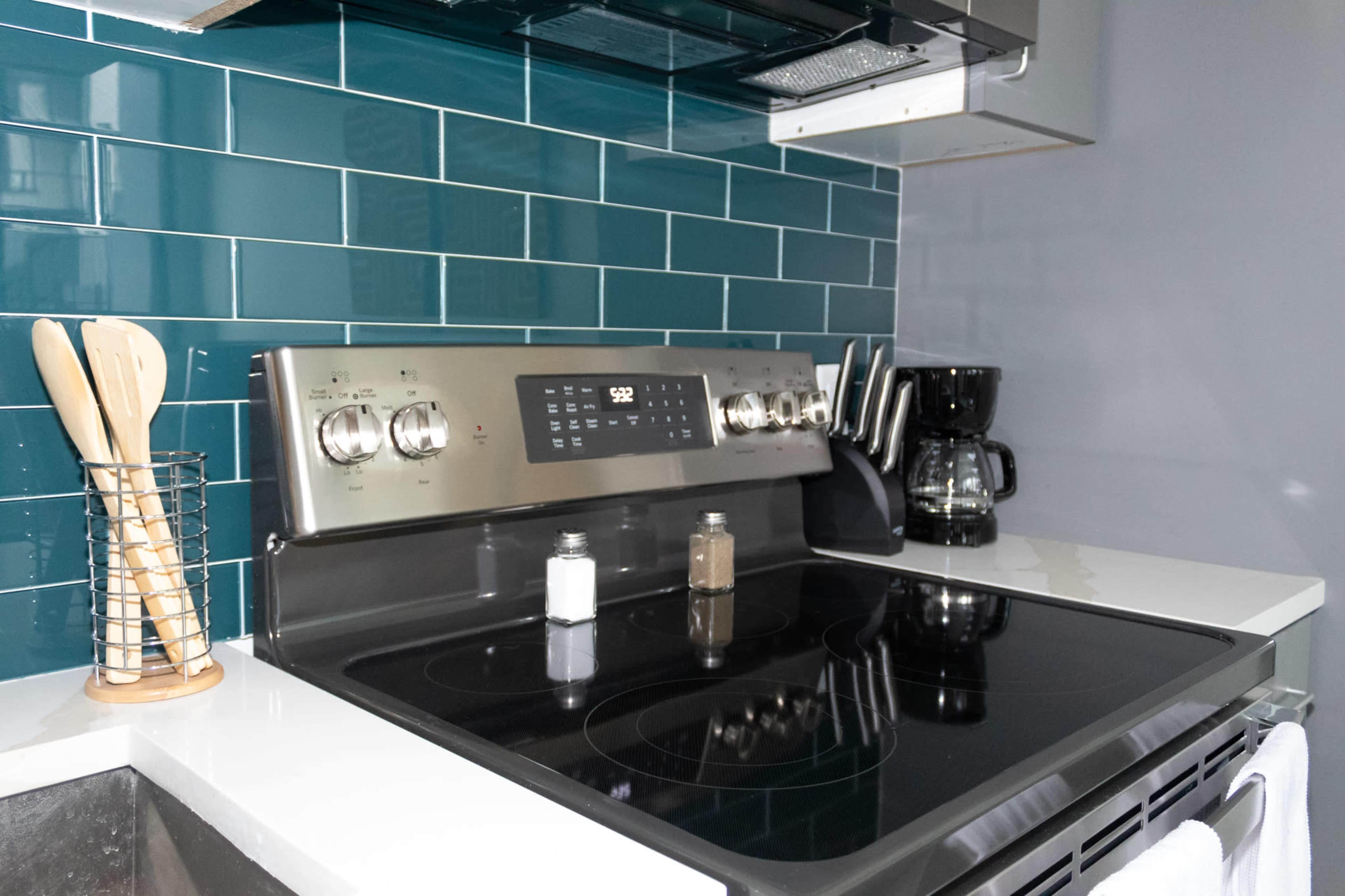 A kitchen countertop with a stainless steel stovetop, black coffee maker, and a rack holding wooden utensils next to salt and pepper shakers.