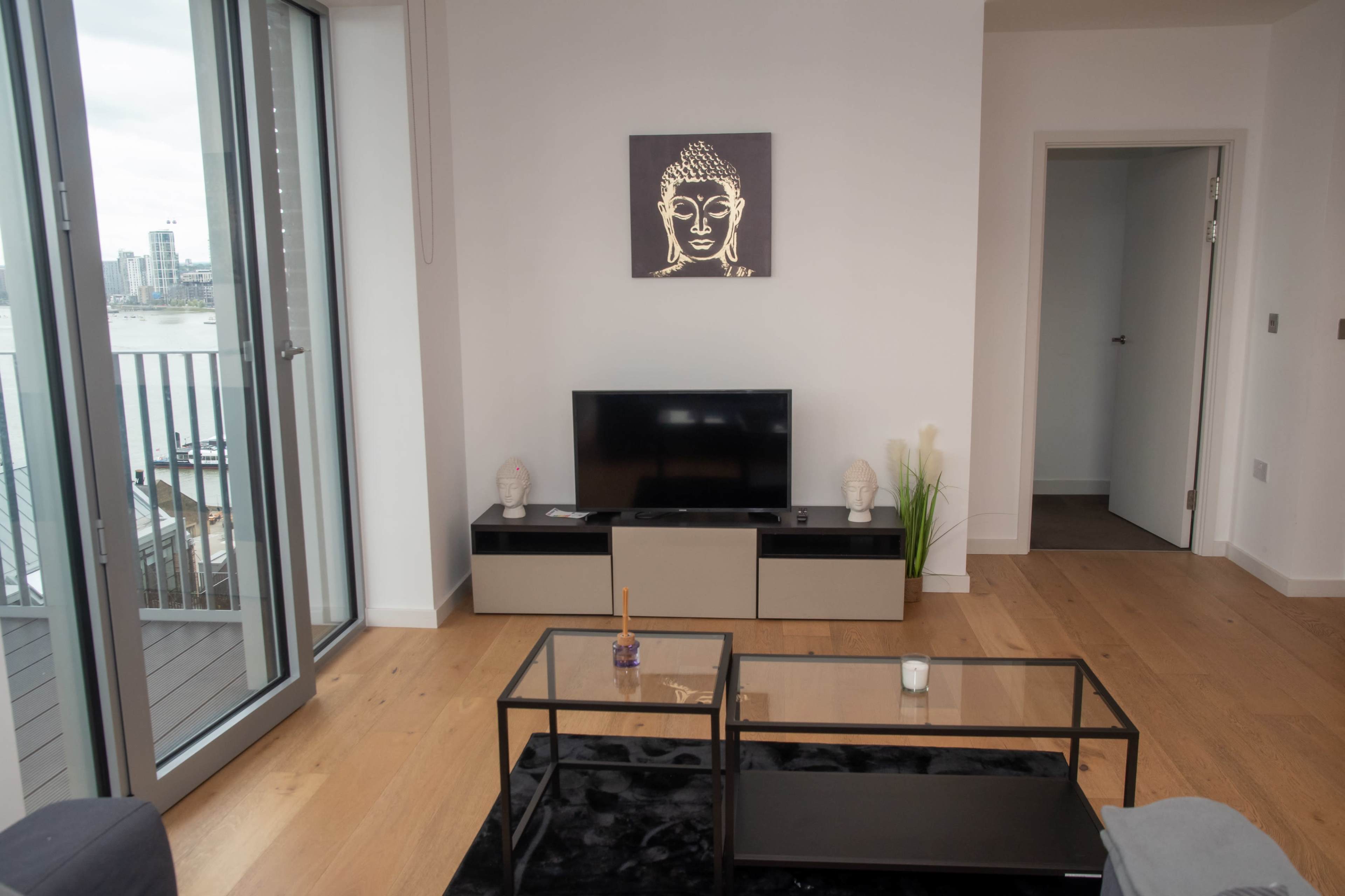 A modern living room with a television on a low cabinet, a coffee table, and a Buddha artwork on the wall.