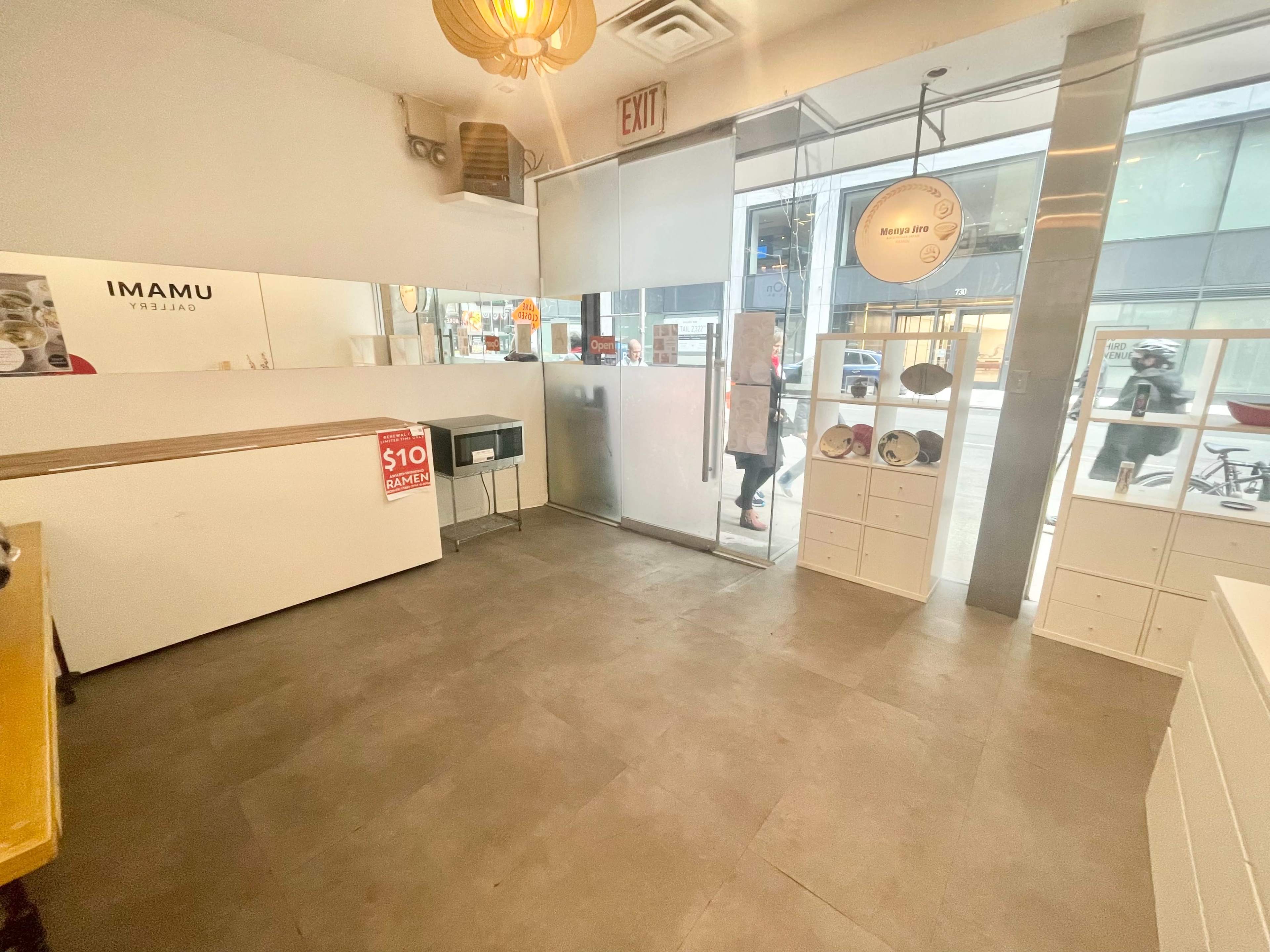 A minimalist interior of a cafe with a white counter, large mirrors, and a glass door leading to the street.