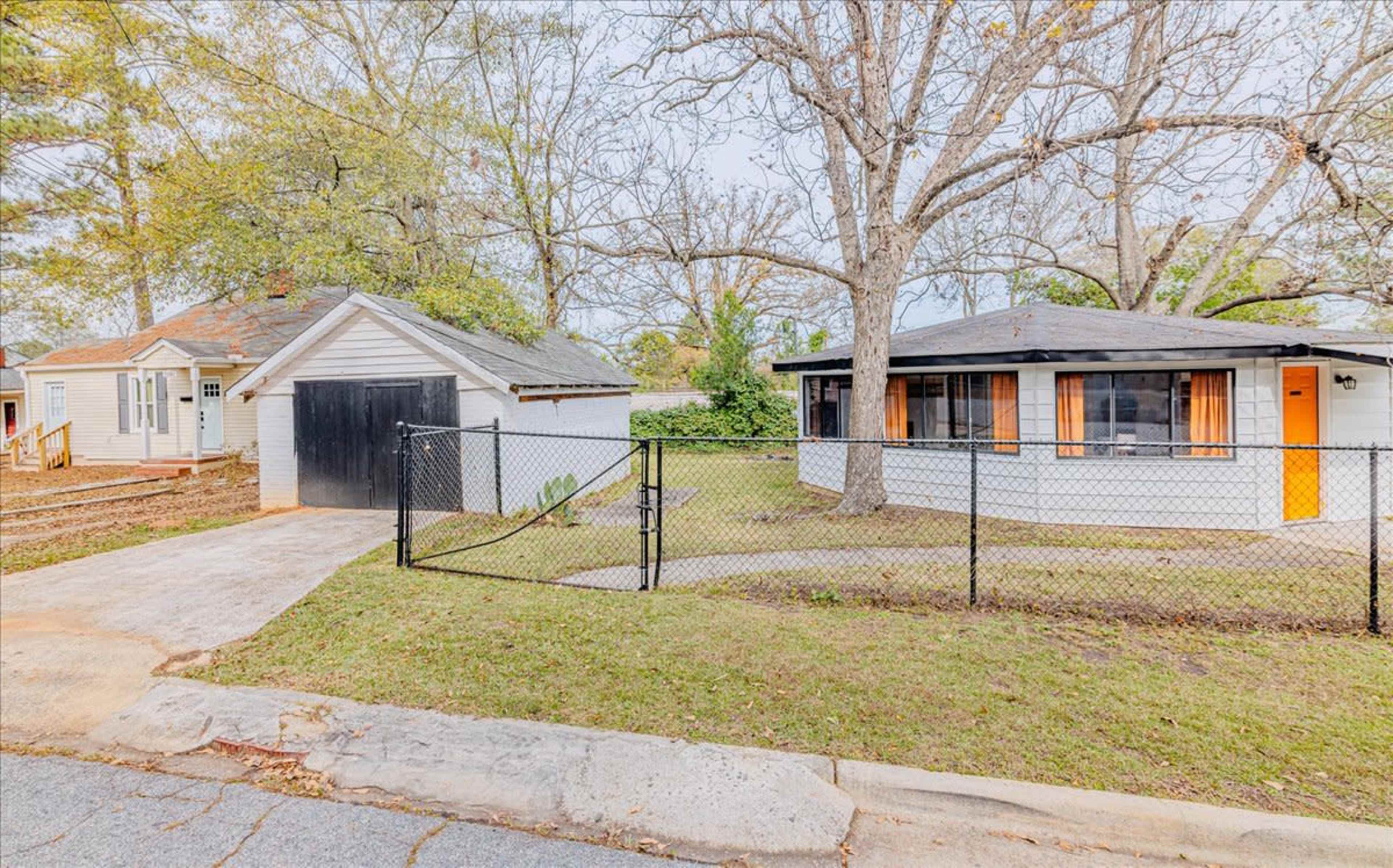 Two houses situated on a grassy lot, with a fenced area in front and a gravel driveway leading to a garage.