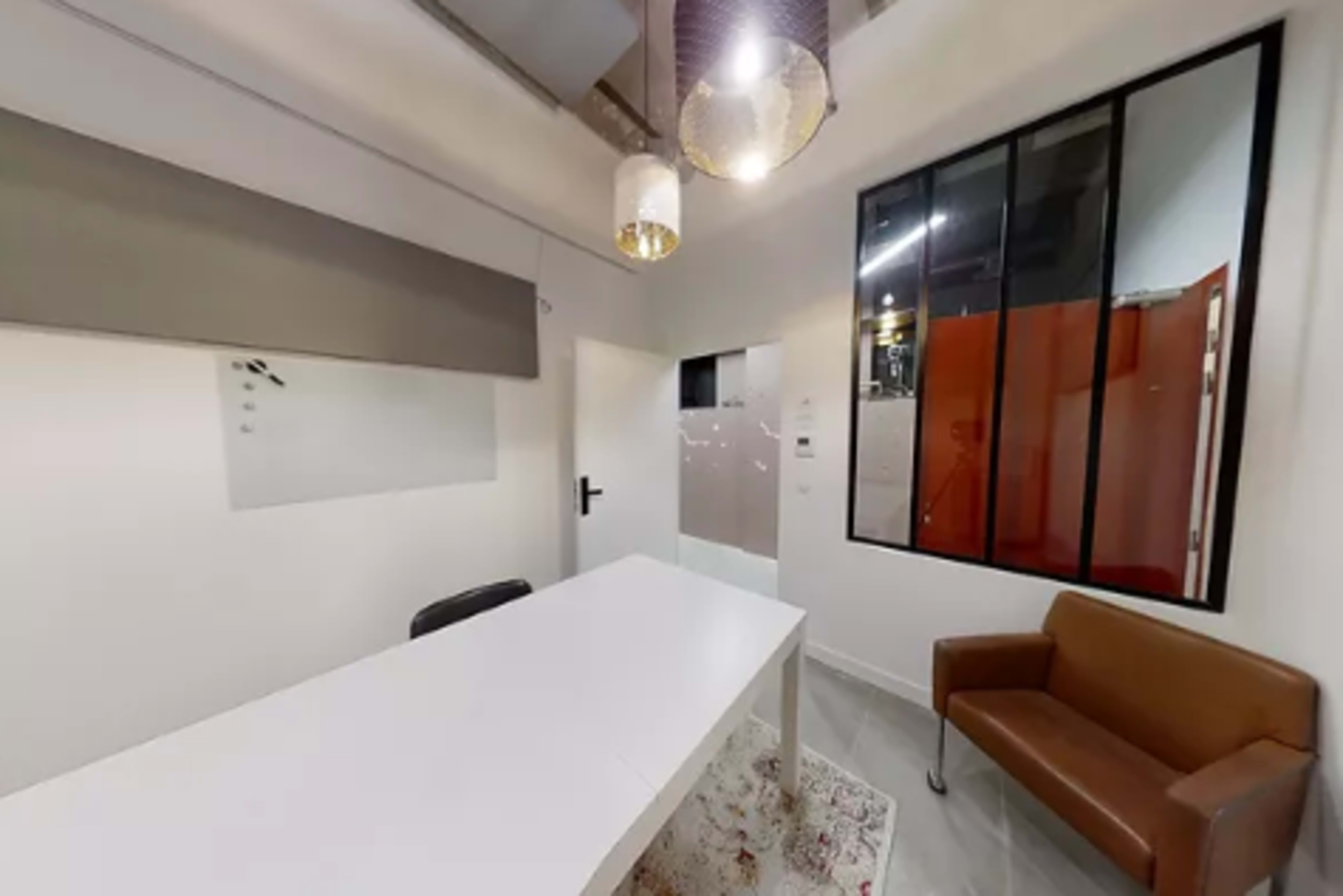 A modern office space with a white table, a brown leather chair, and a large window separating it from an adjacent area.