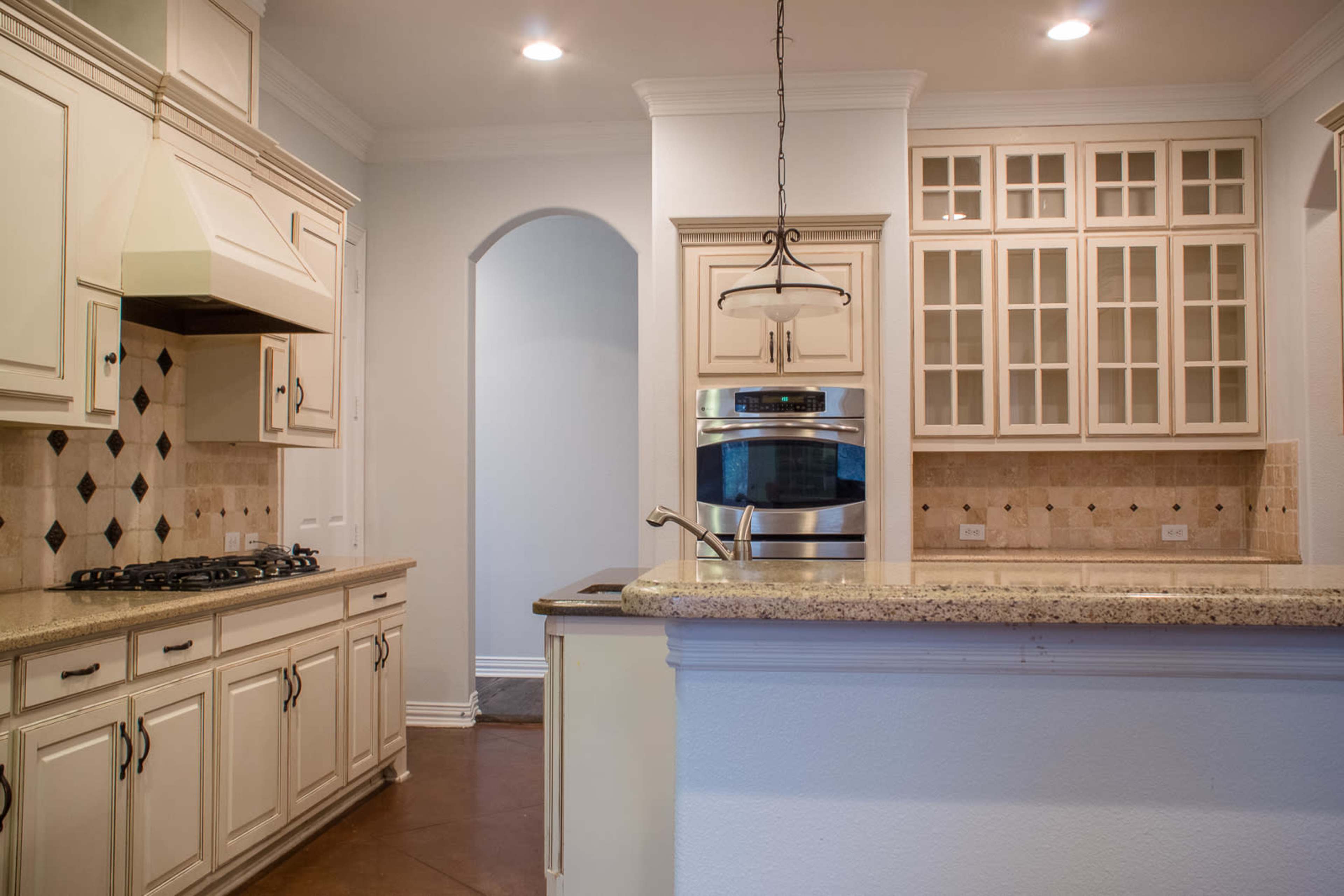 A modern kitchen features light cabinetry, a granite countertop, and stainless steel appliances, with an archway leading to another room.